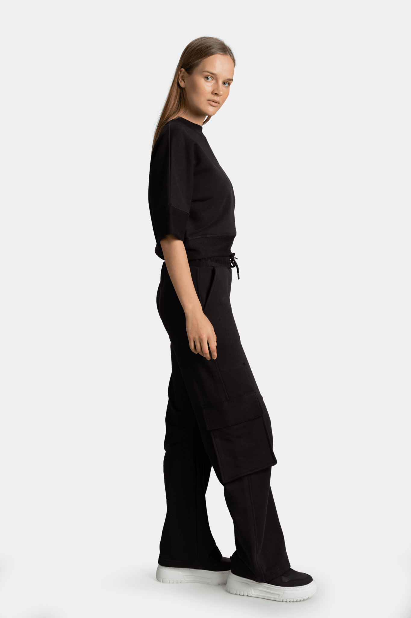 Meira - Cargo Jogger Tracksuit Set in Black, side view displaying the model's profile, focusing on the modern fit and the distinctive cargo pockets on the jogger.