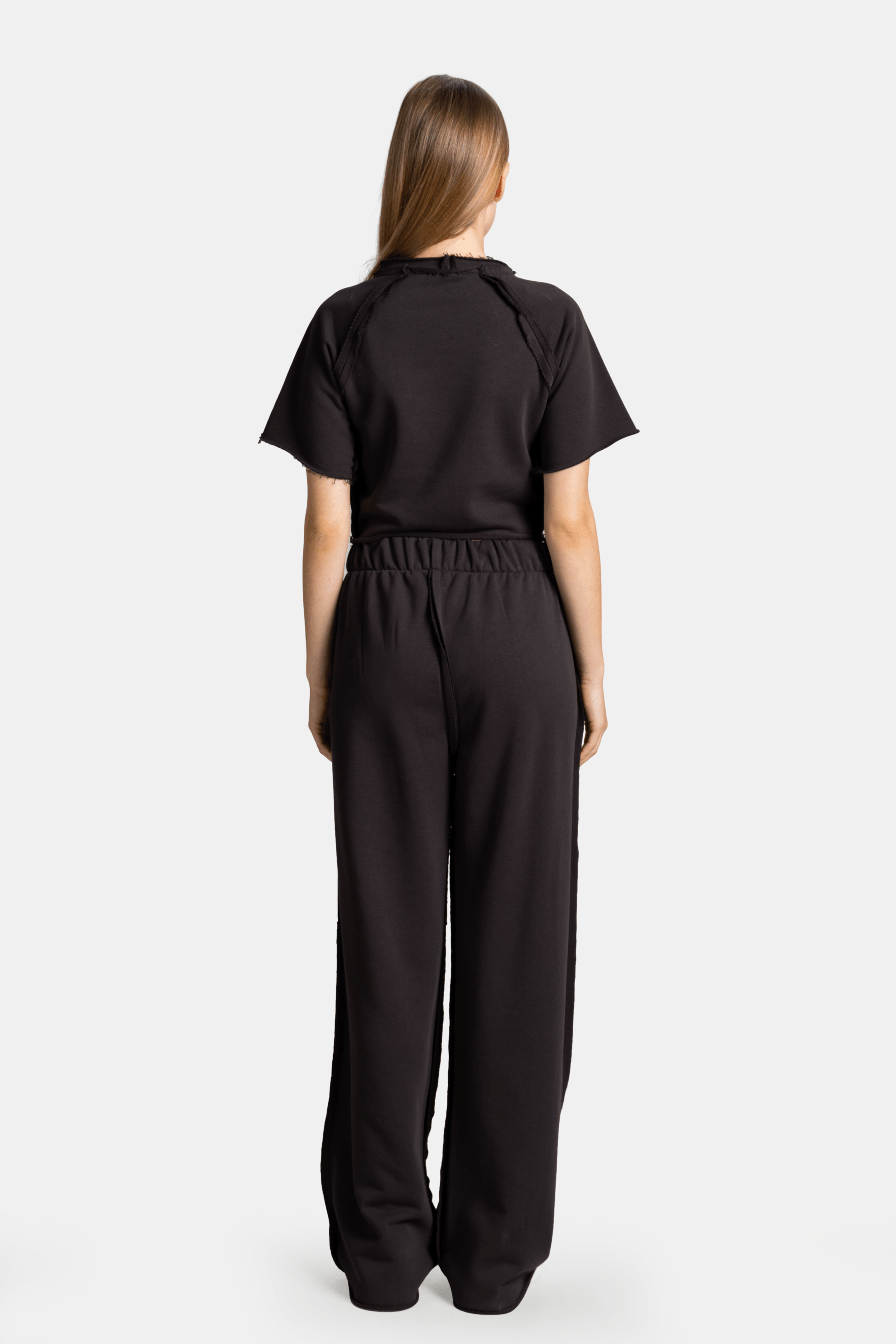 Back view of Amira - Fancy Crop Tracksuit Set in black, highlighting the loose-fit design of the pants and plain back of the crop top.