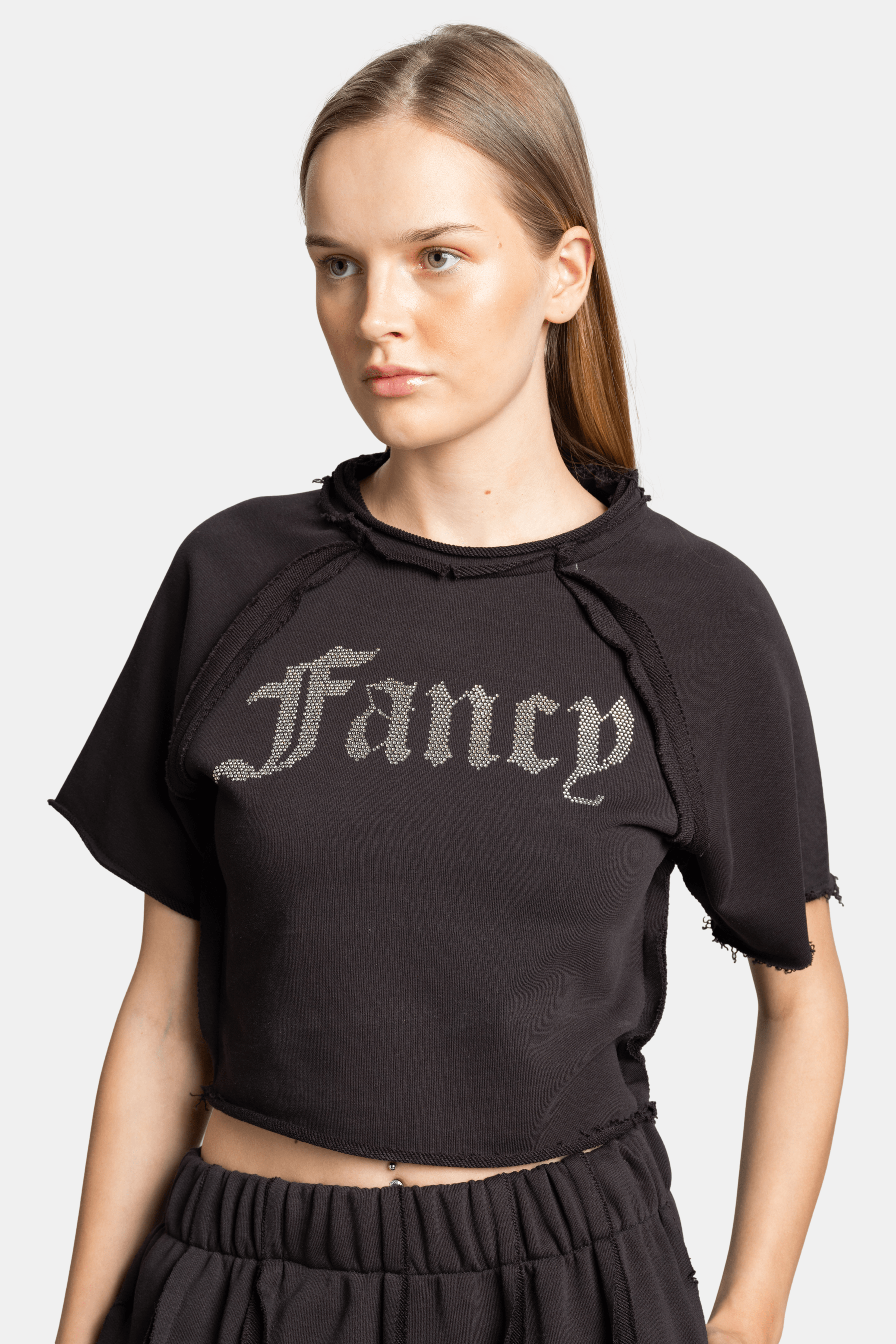 Close-up of the cropped t-shirt in Amira - Fancy Crop Tracksuit Set in black, focusing on the 'Fancy' text design and raw edges.