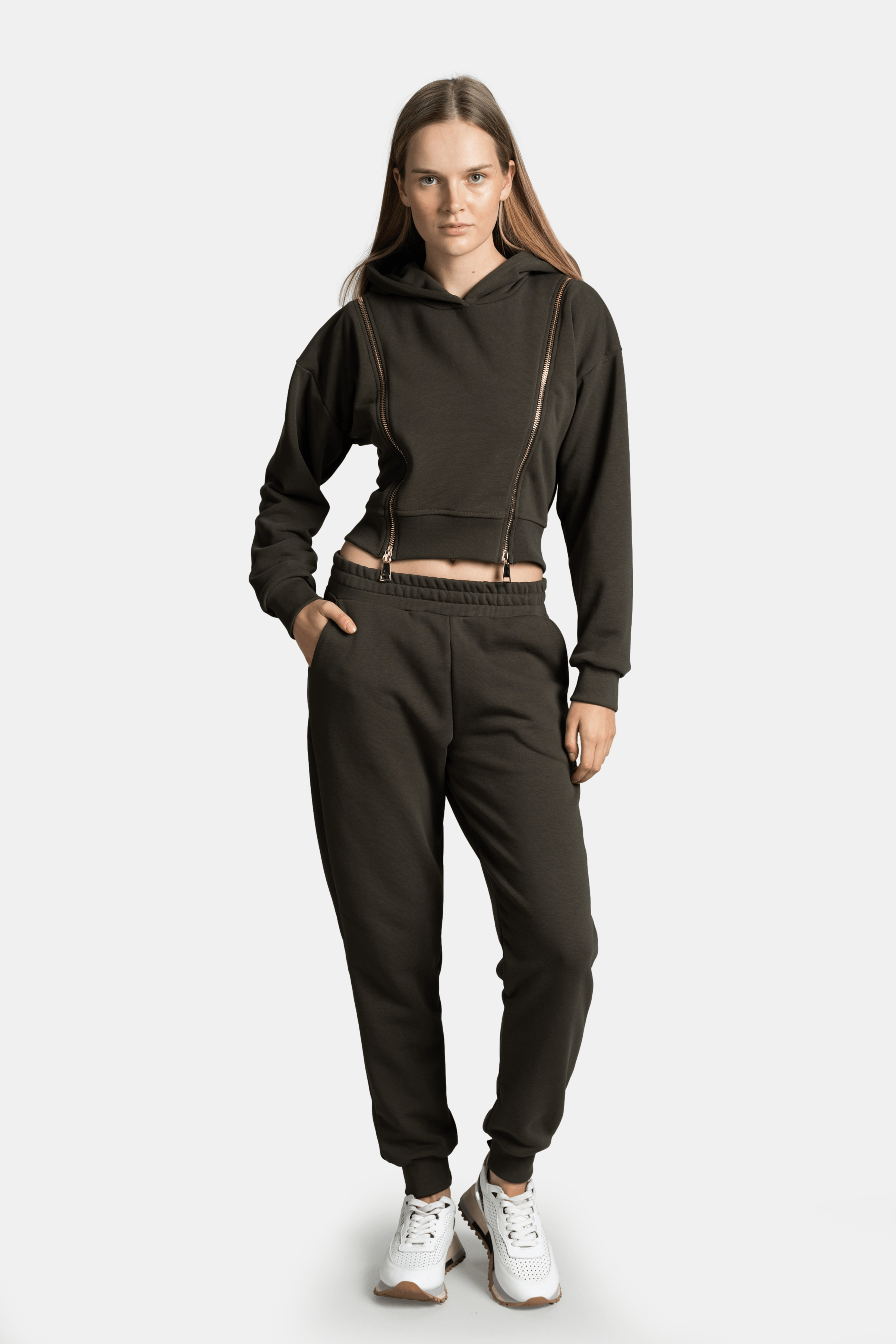 Woman wearing the Amina - Zip Detail Tracksuit Set in khaki, hands in pockets, showcasing the front view of the set with hoodie and jogger pants.