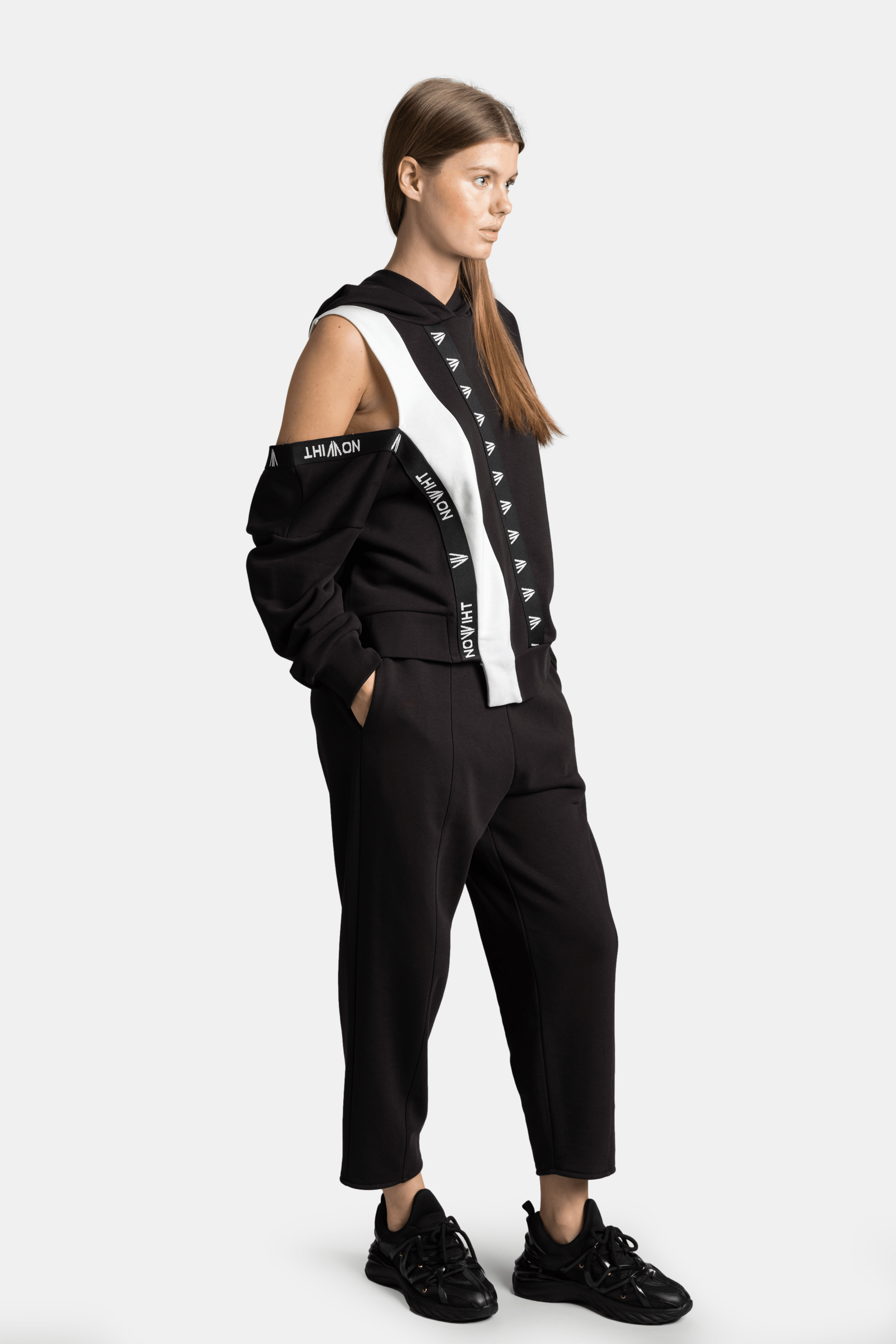 Mira - Cut Out Sleeve Tracksuit Set in Black, side view highlighting the stylish cut-out sleeve and branded stripe on the black tracksuit.