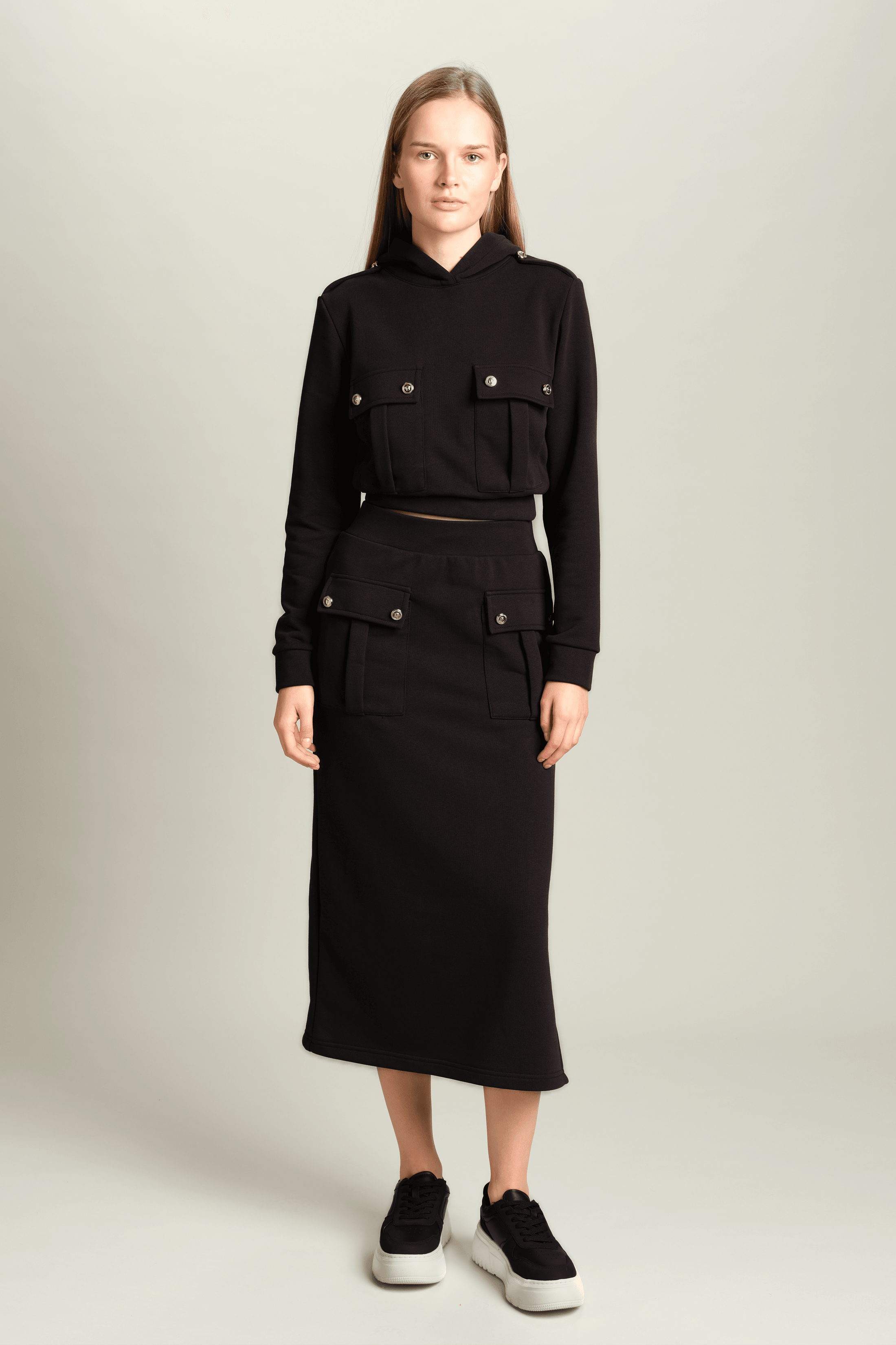 Capri - Pocket Detail Skirt Set in Black, front view displaying the chic black hoodie and matching skirt with detailed front pockets, model posing with a relaxed stance.