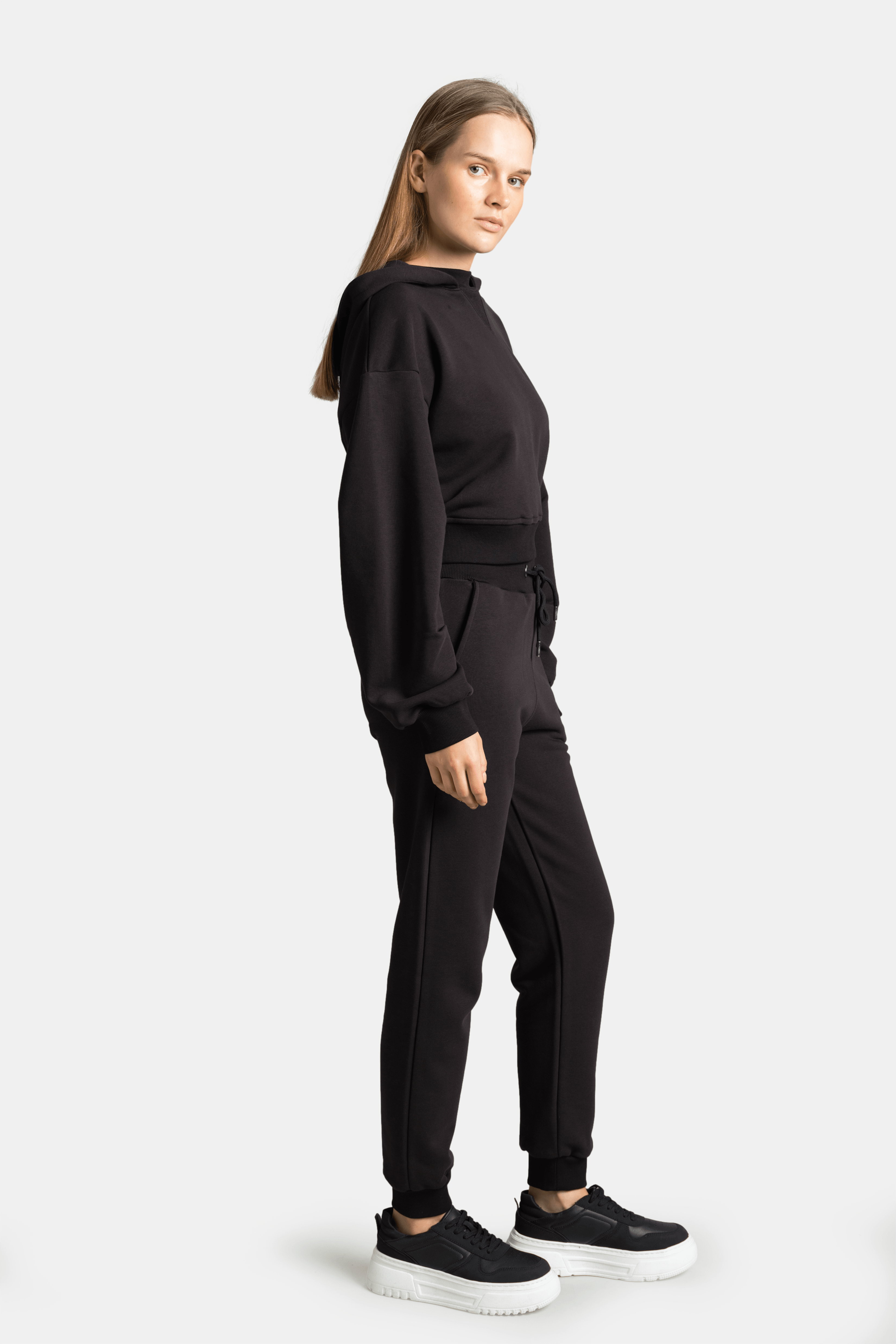 Model adjusting hood in the Lilot Tone on Tone black tracksuit set, featuring sleek and understated styling