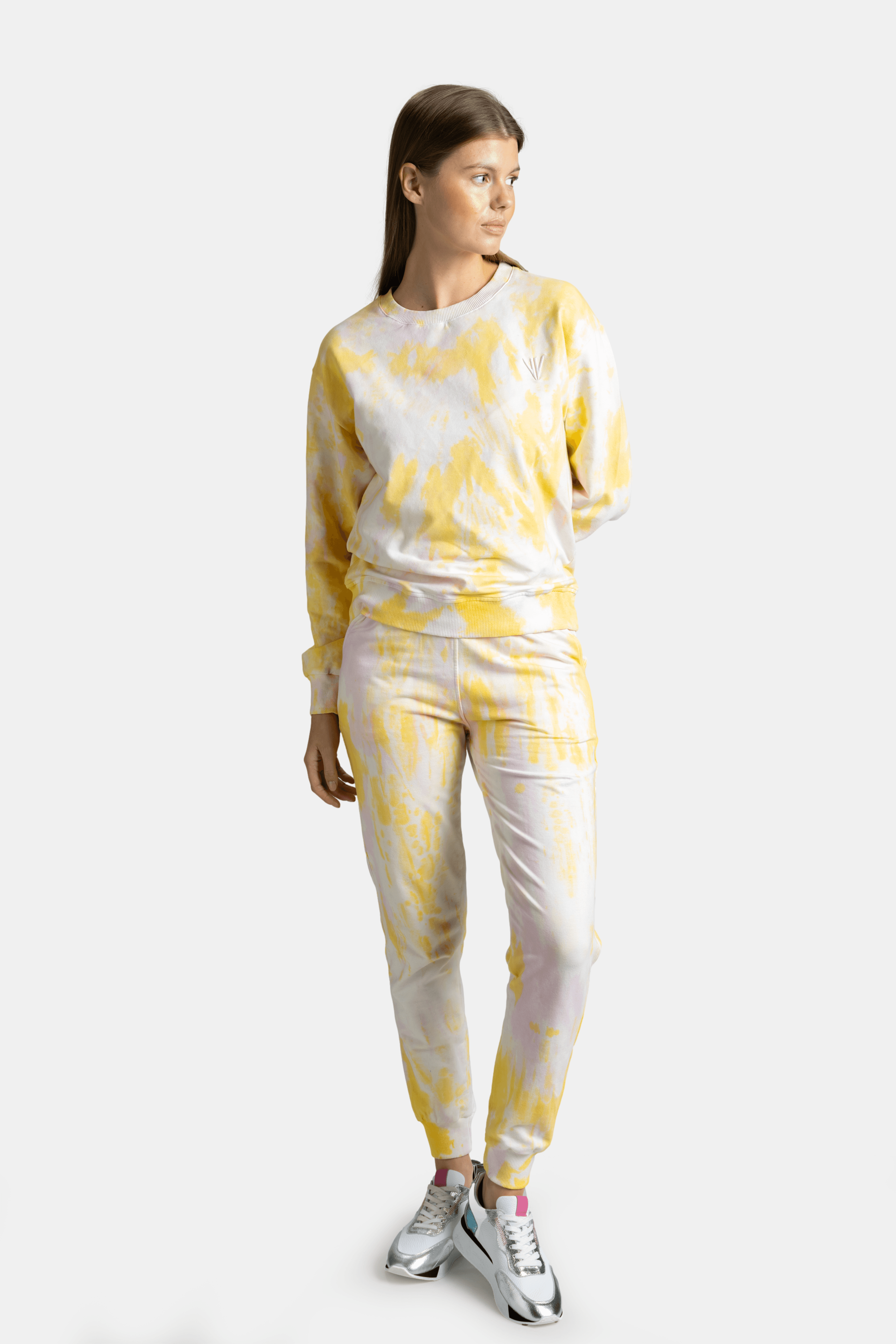 Woman in a yellow tie-dye tracksuit, facing slightly sideways, with relaxed posture and casual expression.