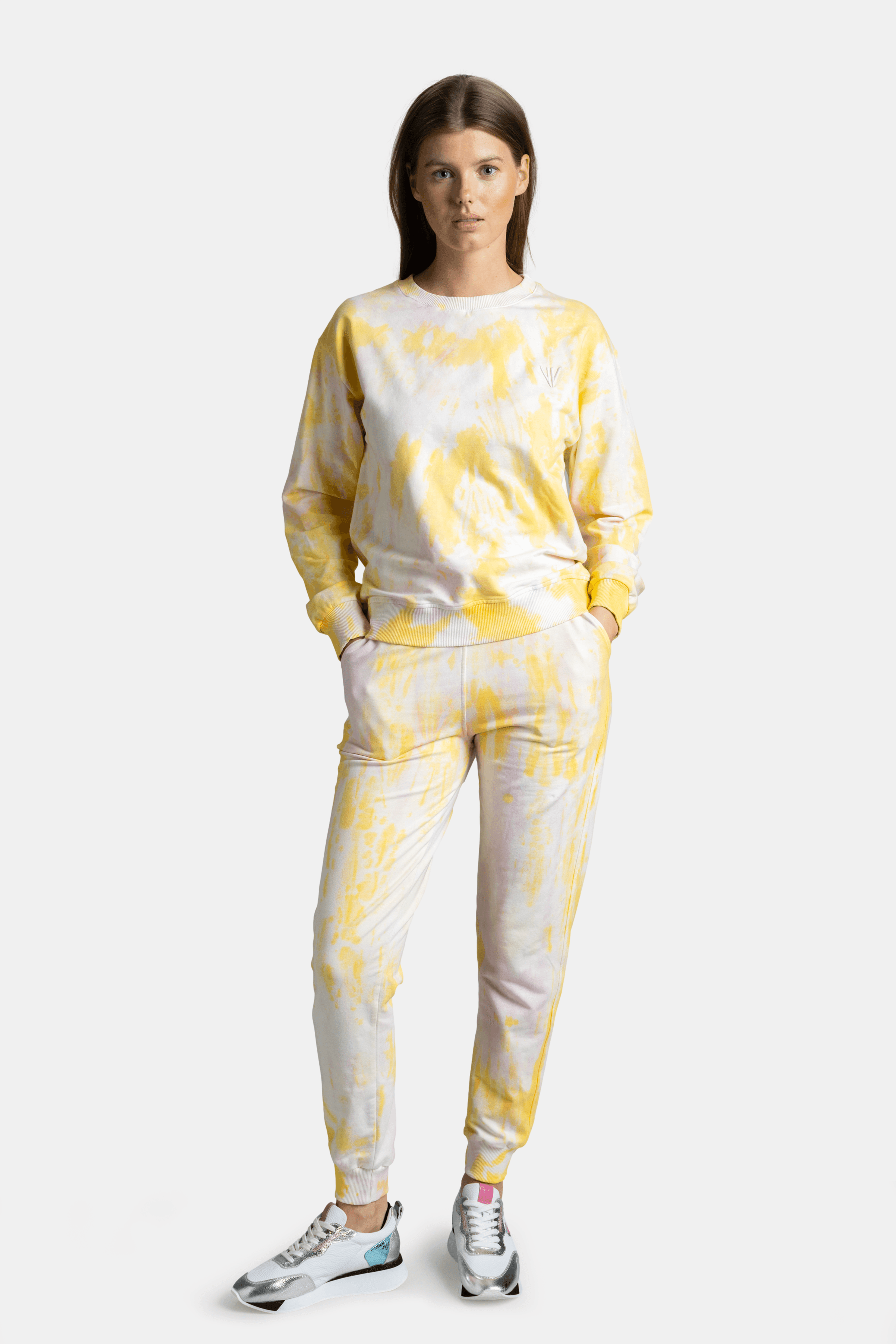 Woman wearing a yellow tie-dye tracksuit, front view, hands in pockets, looking directly at the camera.