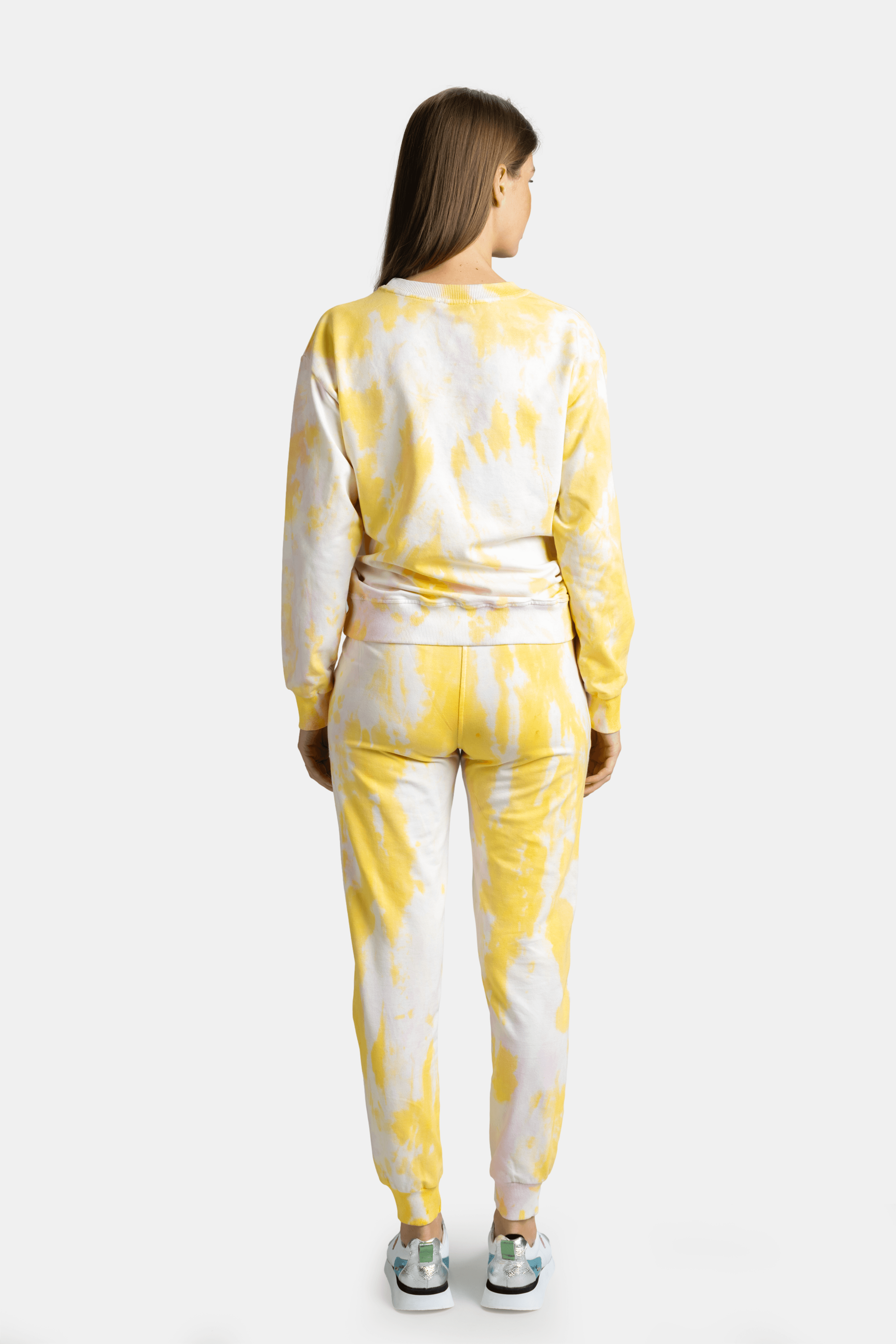 Rear view of a woman wearing a yellow tie-dye tracksuit, with her hands relaxed by her sides.