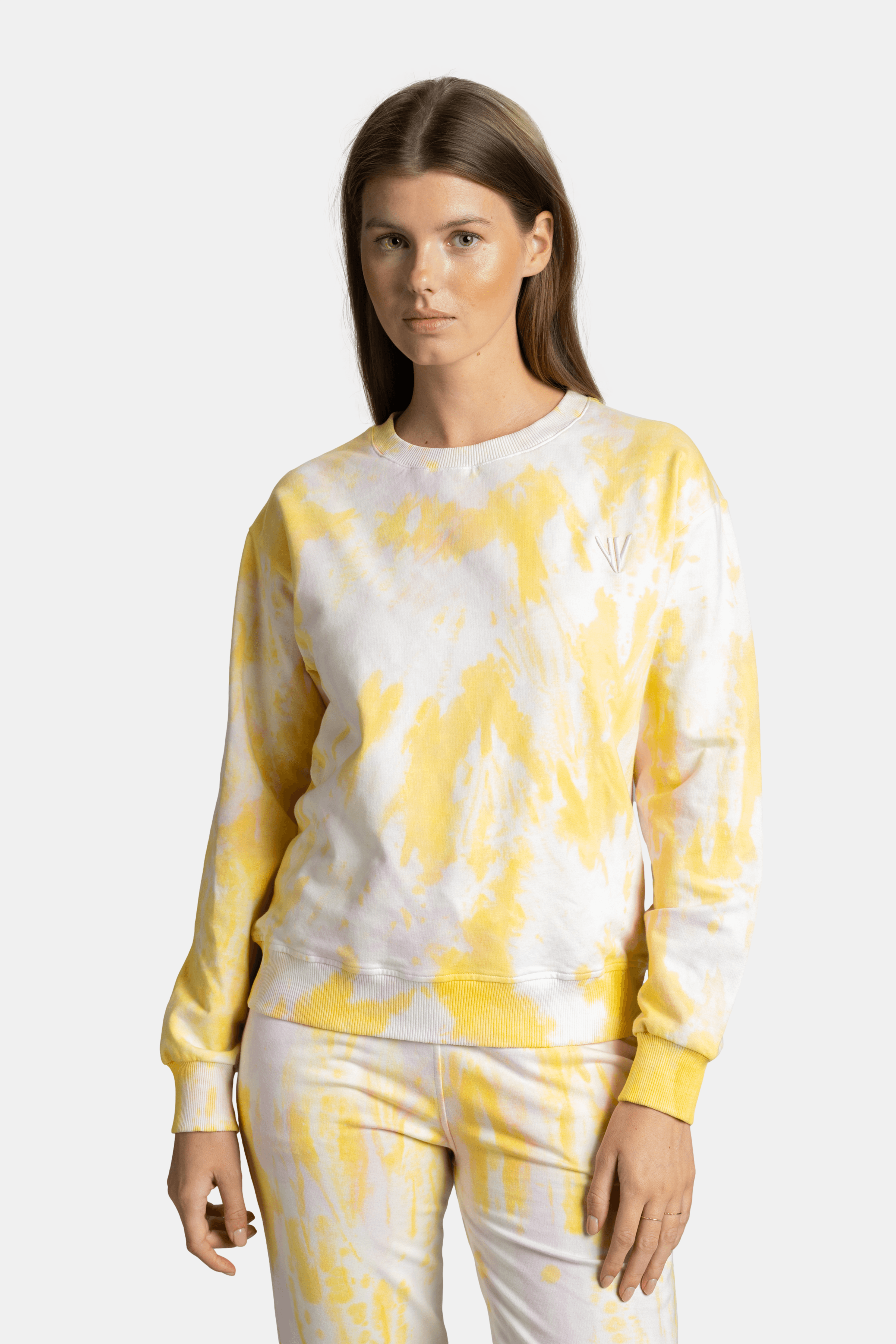 Close-up of the upper half of a yellow tie-dye tracksuit with subtle logo detail on the chest.