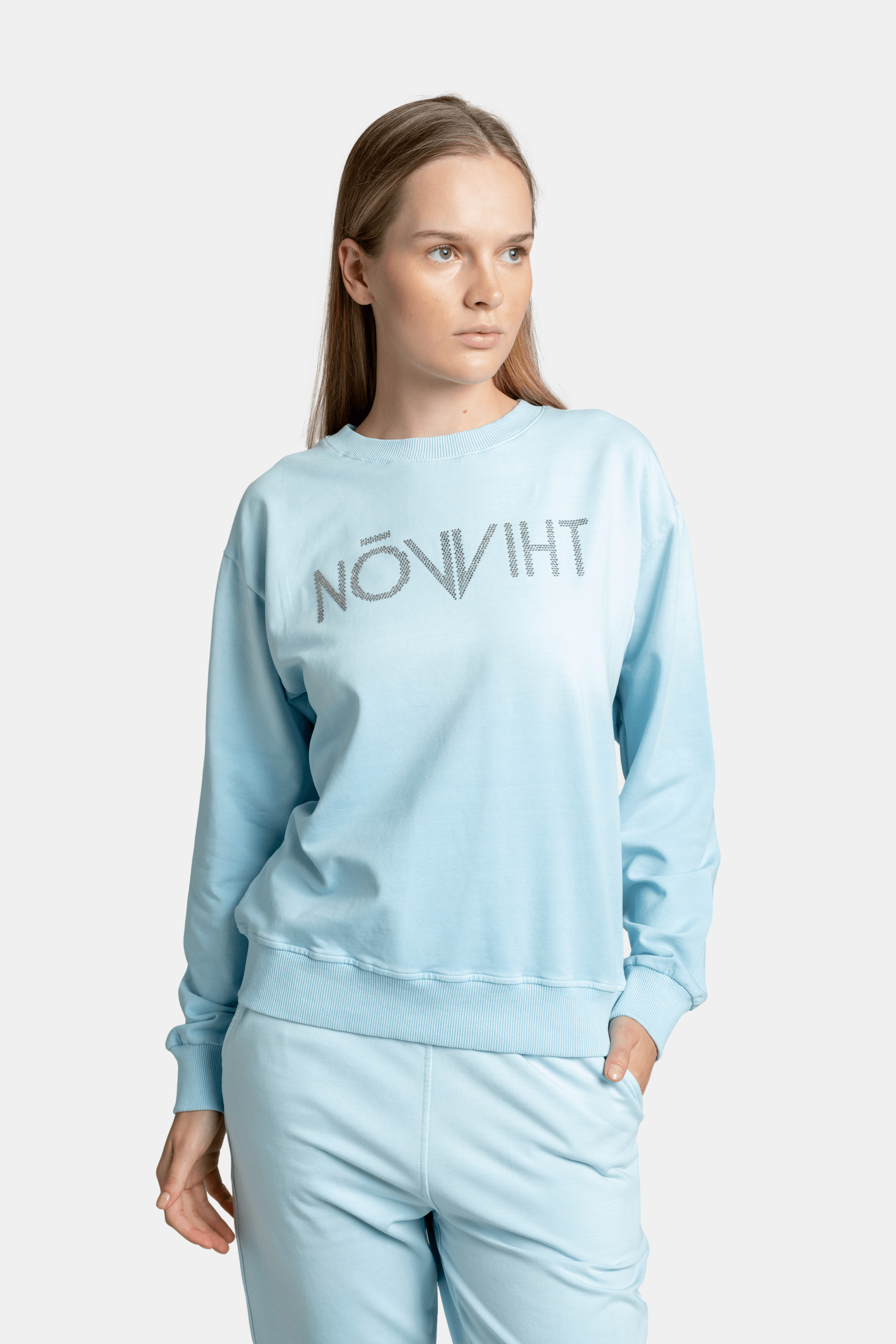 Close-up of the light blue sweatshirt featuring the NOWIHT logo in rhinestone detail, worn by a woman.