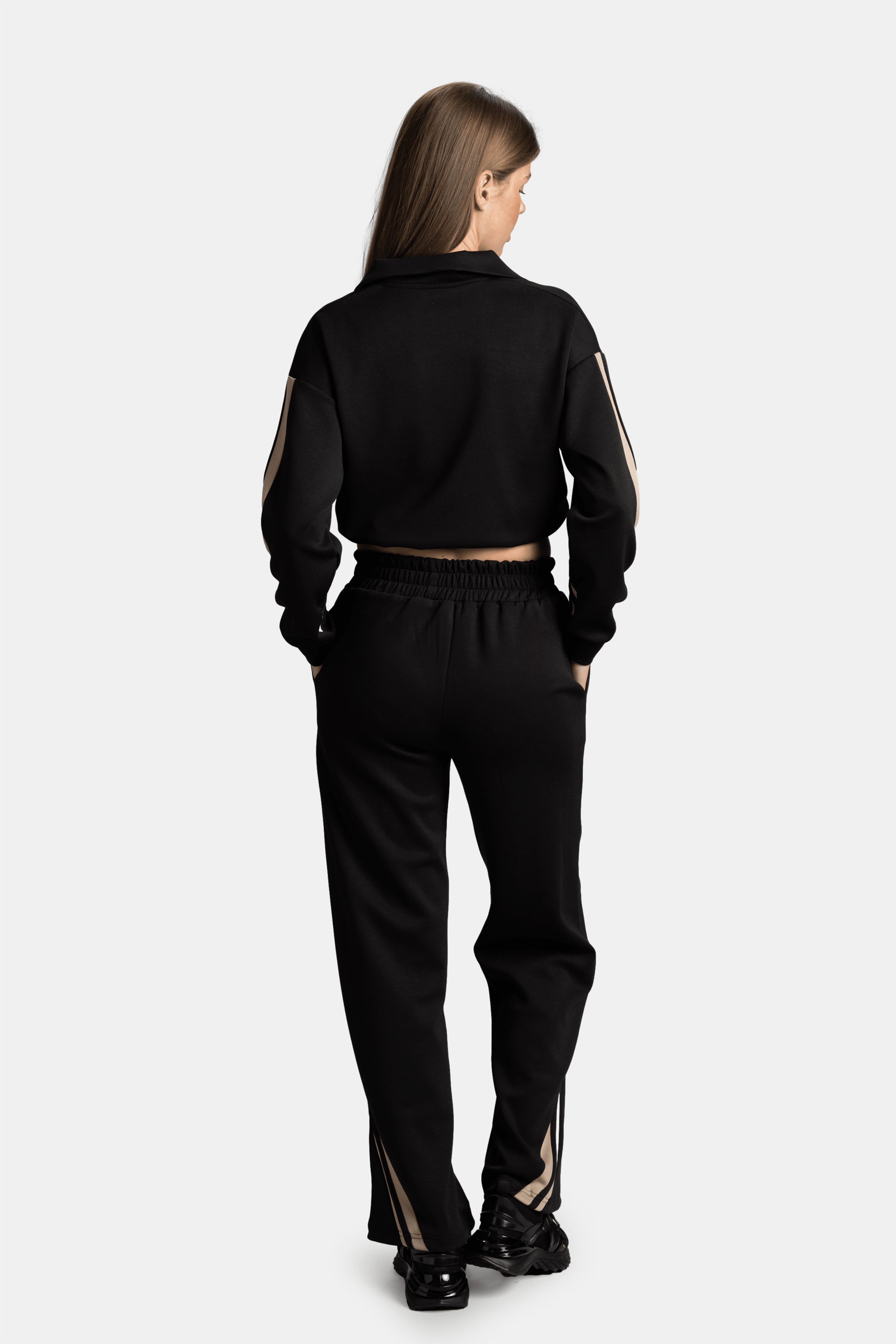 Rear view of the model in a black tracksuit with beige stripes on the sleeves and pants, showcasing the back design and loose fit.