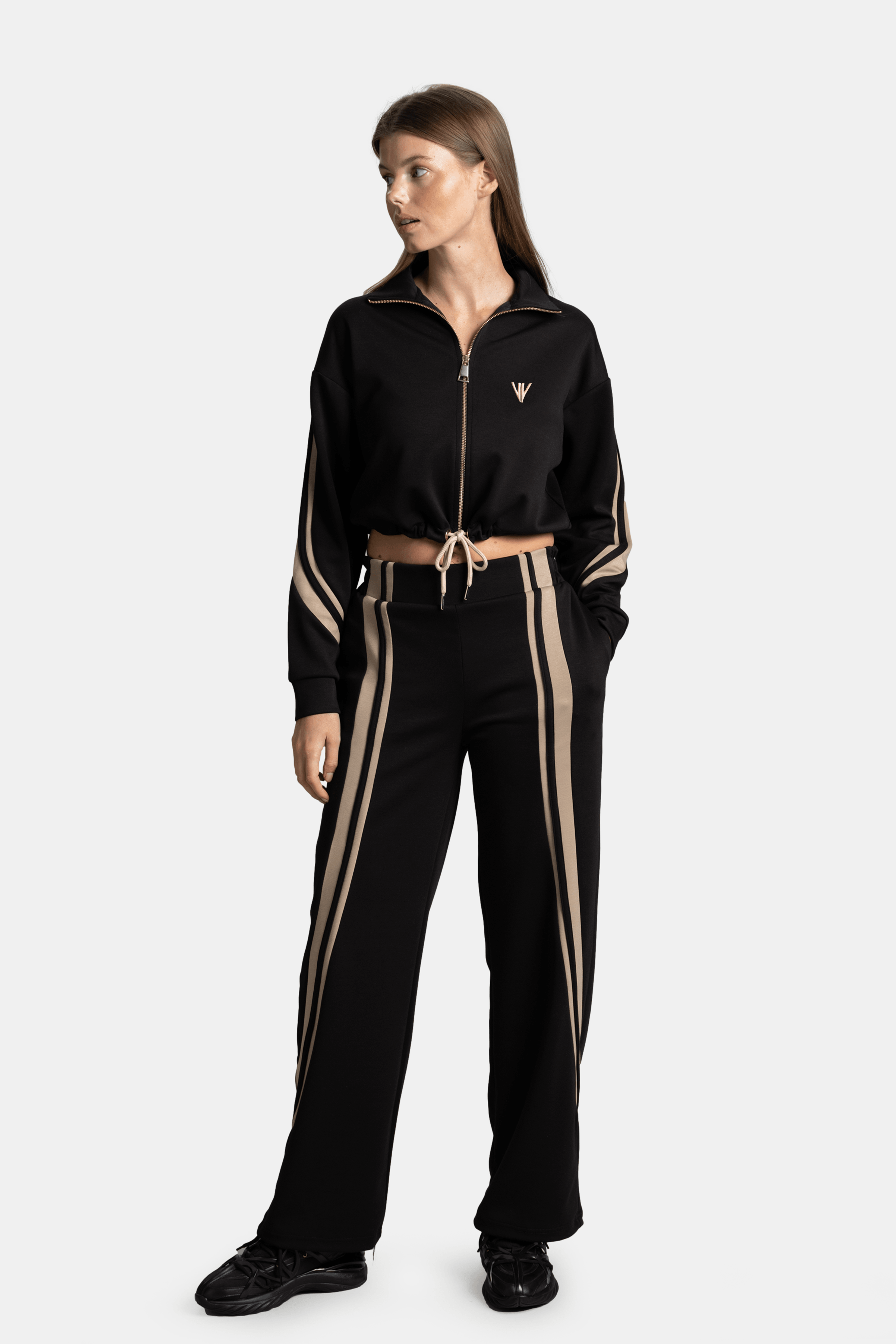 A model in a black and beige striped tracksuit, looking to the side with a relaxed stance, highlighting the zip-up top and drawstring waist.