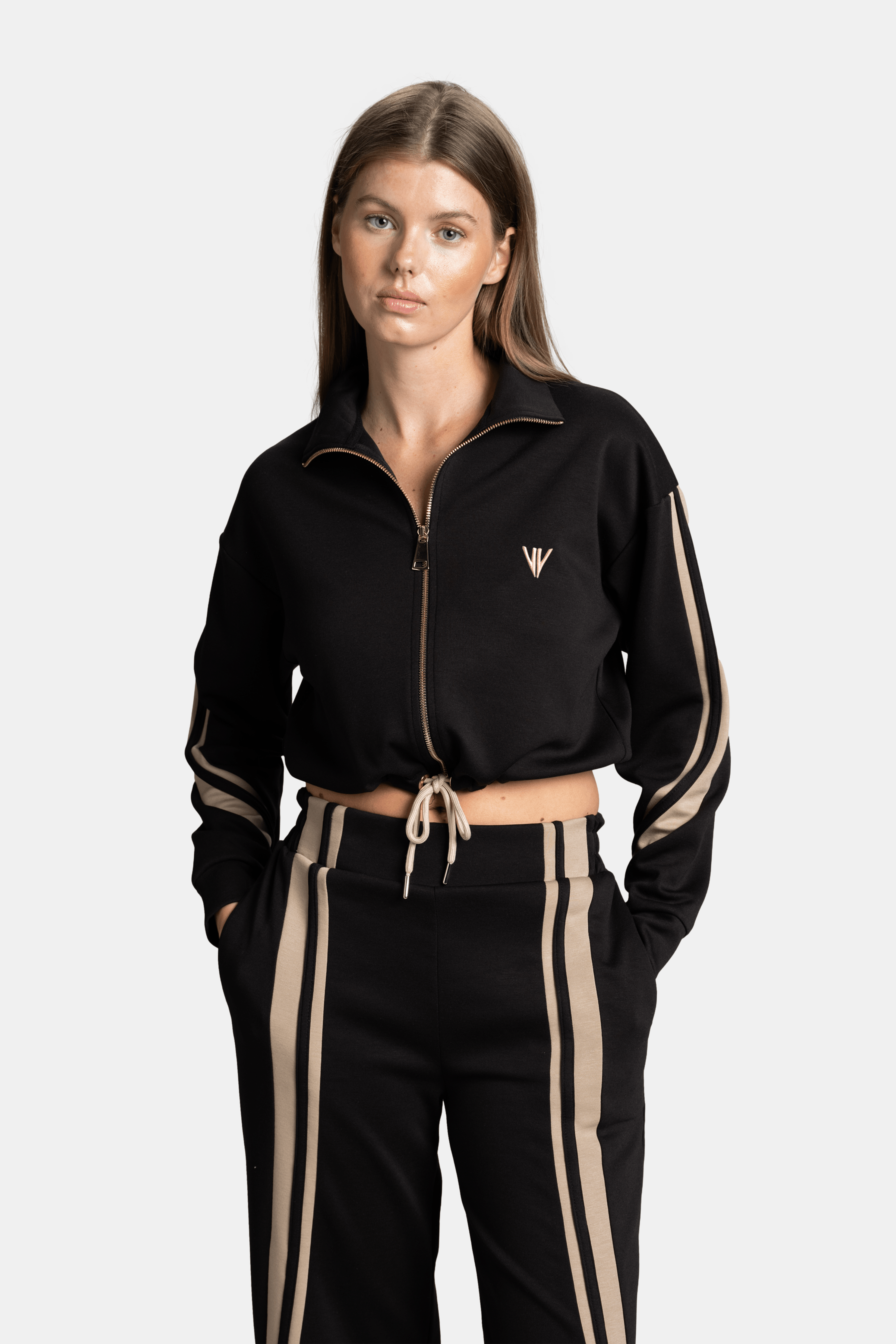 Front view of the model in a black tracksuit with beige stripes, with arms slightly bent, showcasing the full outfit’s fit and design.