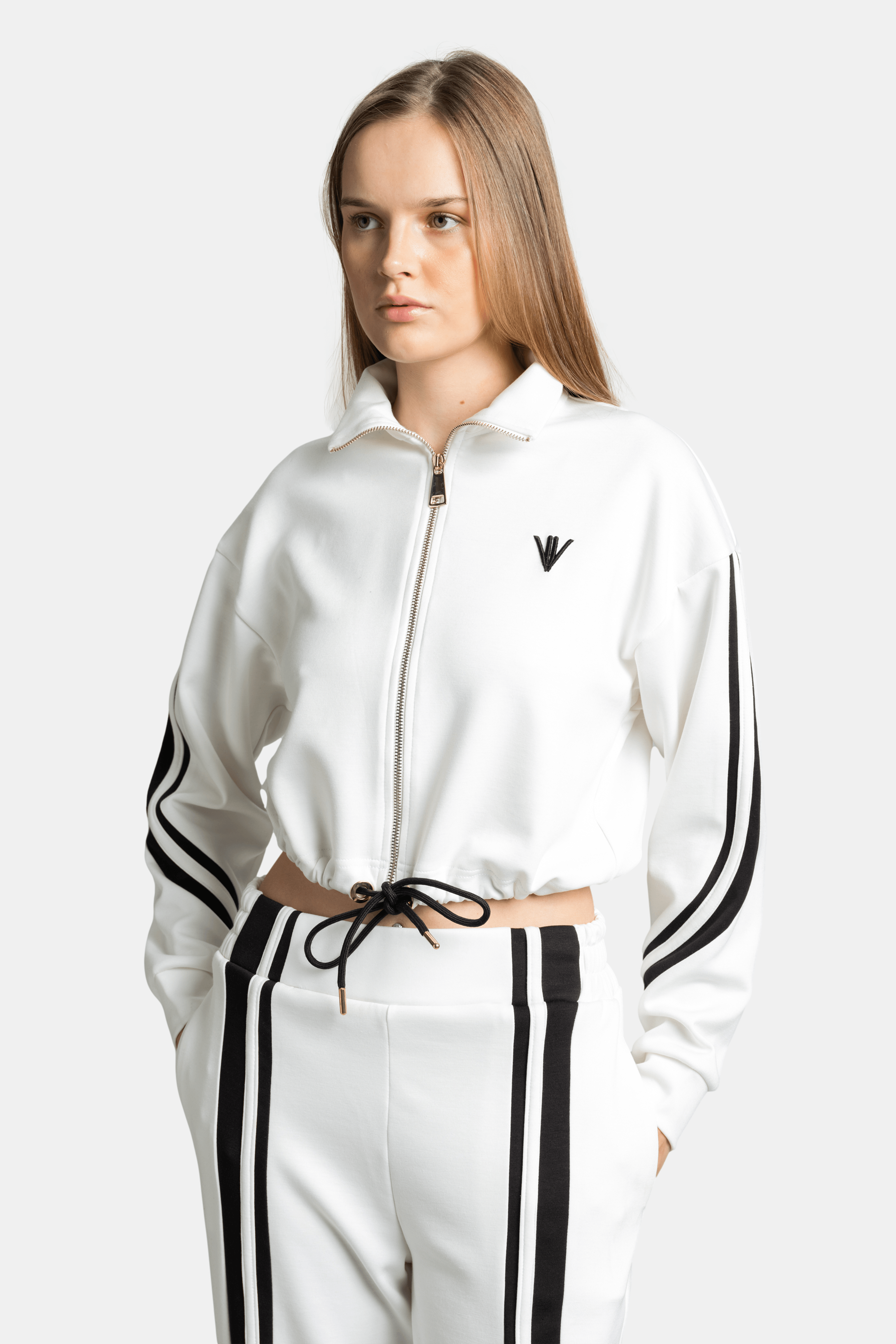 Close-up of a woman in a white zip-up tracksuit top with black side stripes, focusing on the top's drawstring and logo detail.