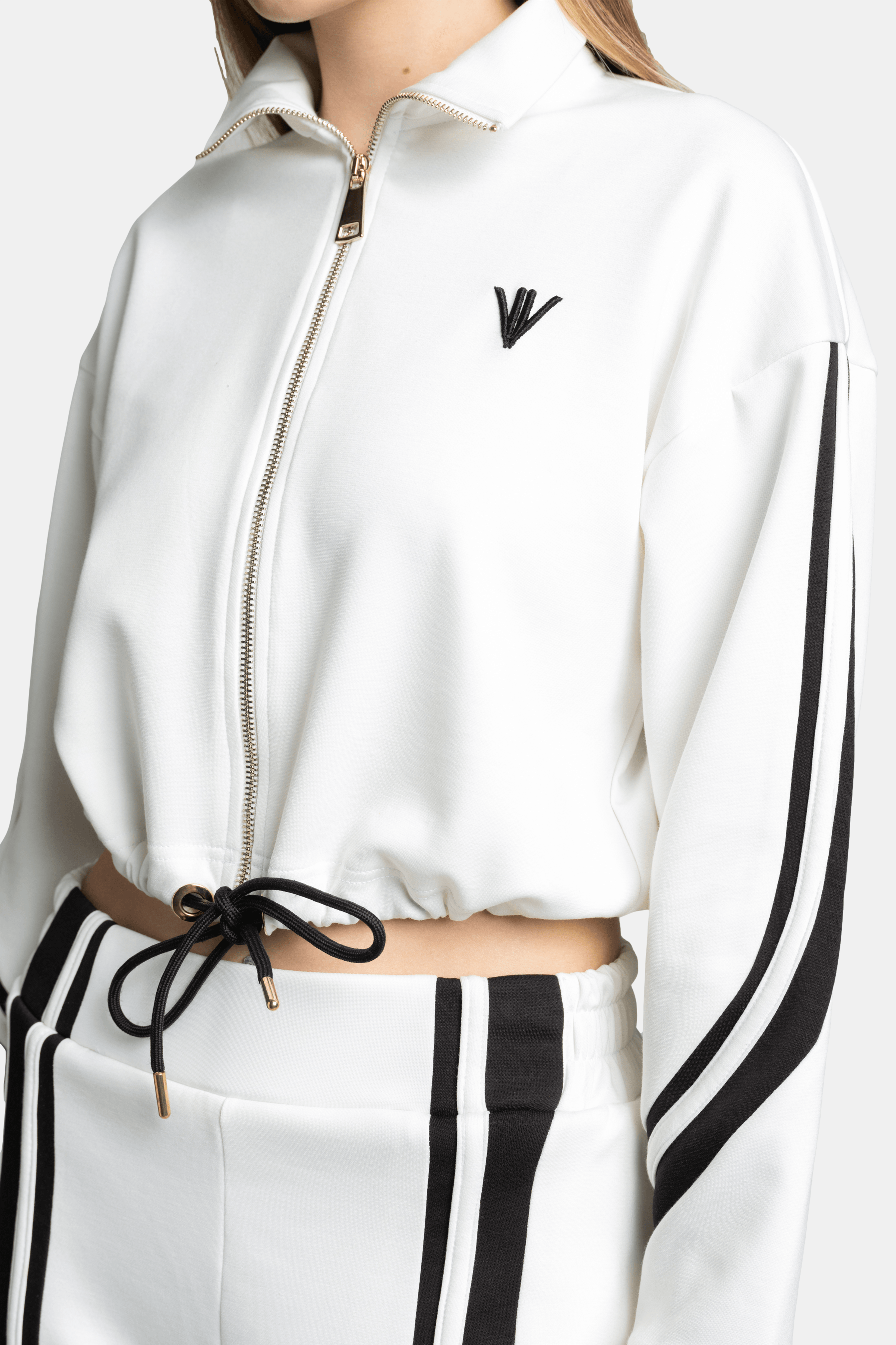 Detail of the woman’s waist area in a white tracksuit set, showing the black side stripes and drawstring waist.