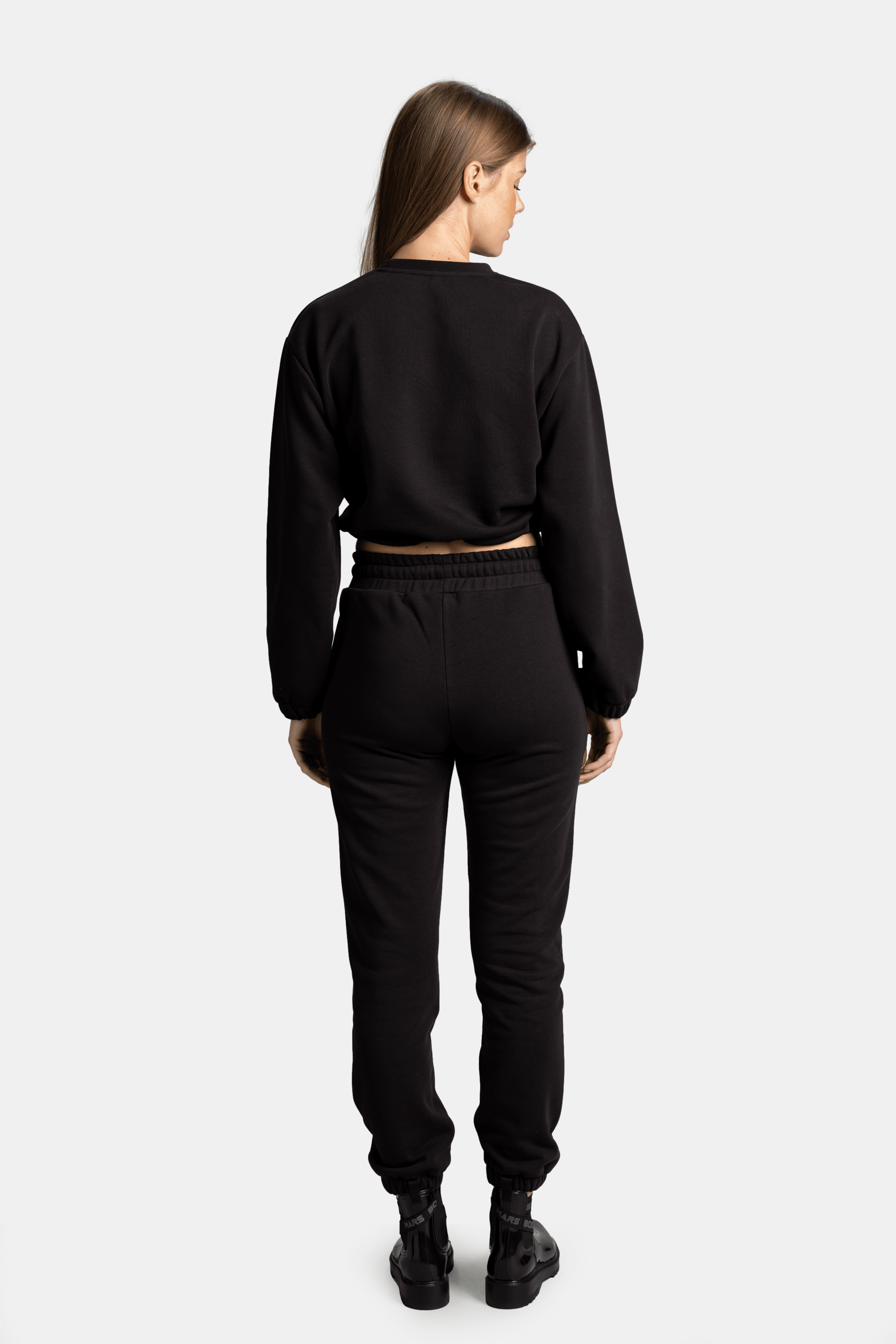 A back view of the woman wearing the black sweatshirt and pants, showing the relaxed fit of the set and the elastic waistband of the pants.