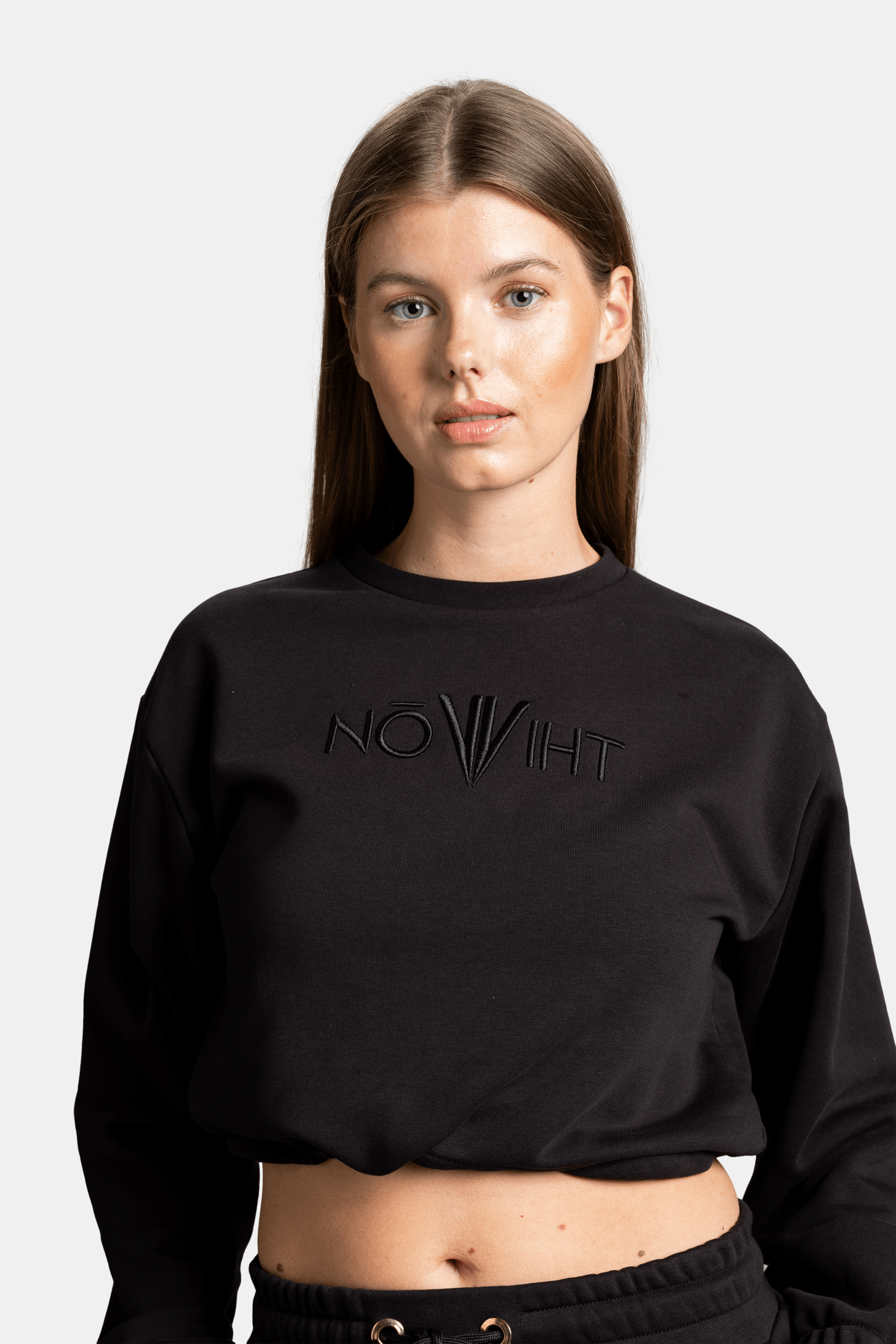 A close-up of the woman wearing the black NOWIHT sweatshirt, showcasing the embroidered logo on the chest and the drawstring detail at the waist.