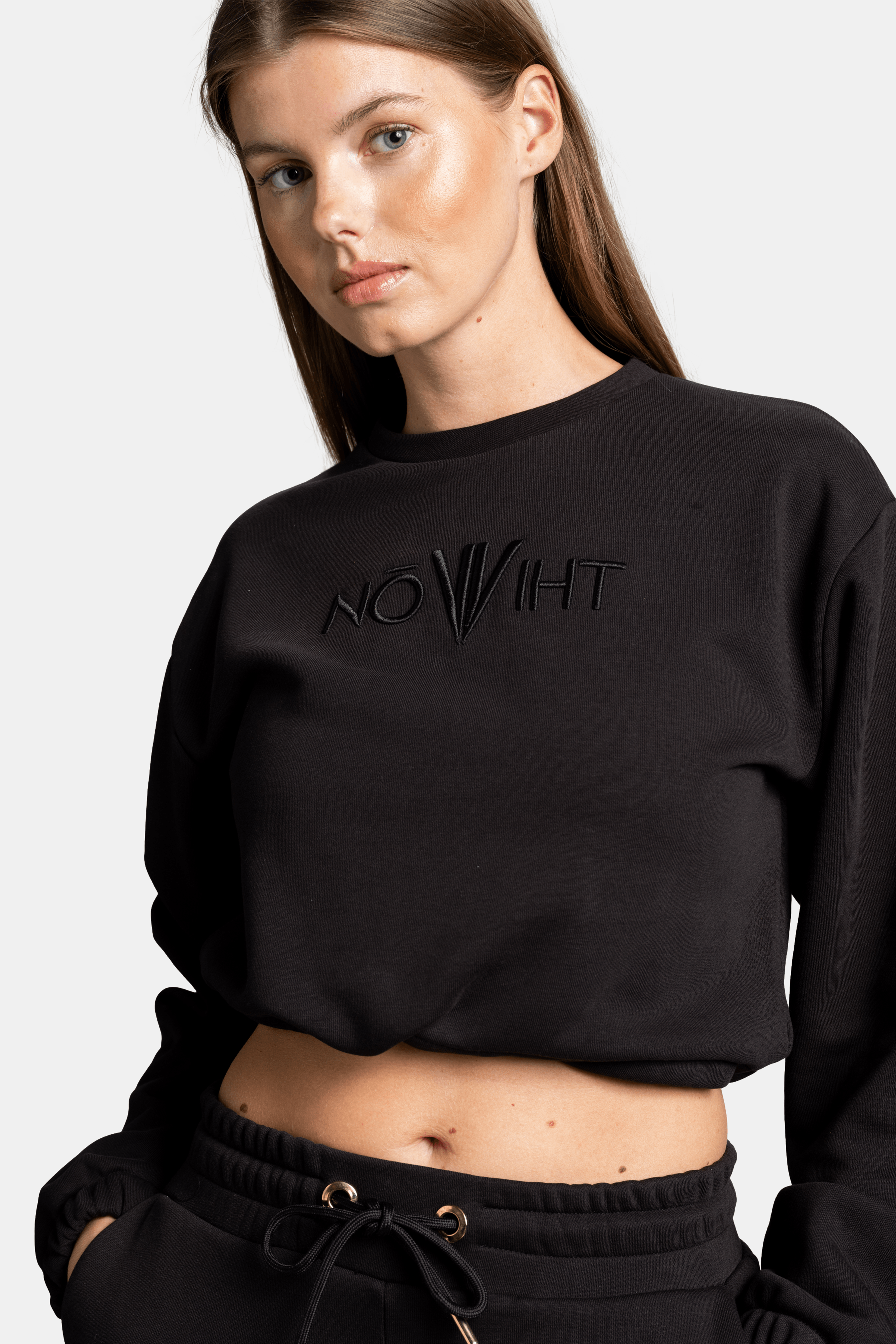 A close-up side view of the woman in the black NOWIHT sweatshirt, focusing on the embroidered logo on the chest and the texture of the fabric.