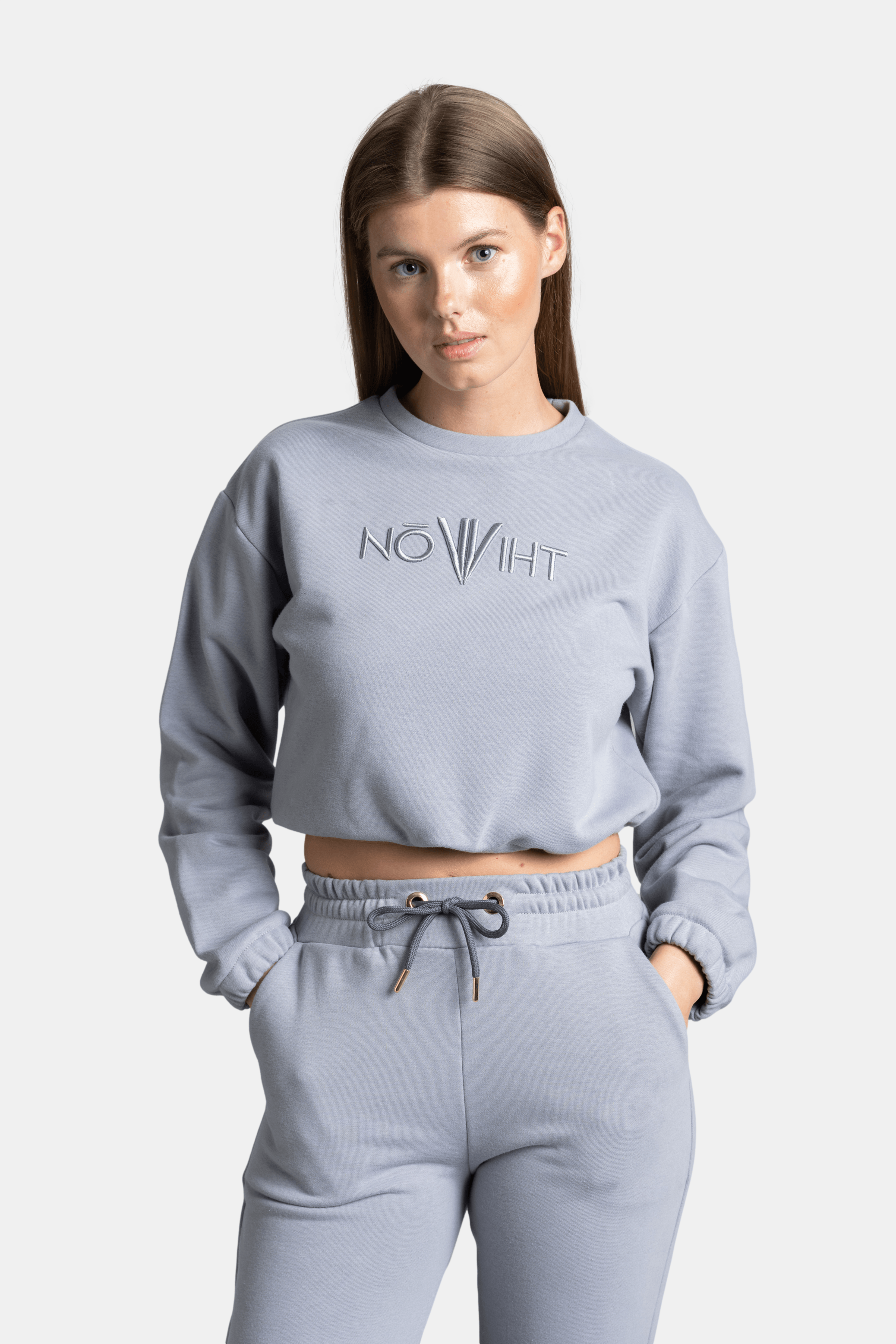 Close-up of woman in light gray NOWIHT tracksuit set, showing logo on sweatshirt and drawstring details.