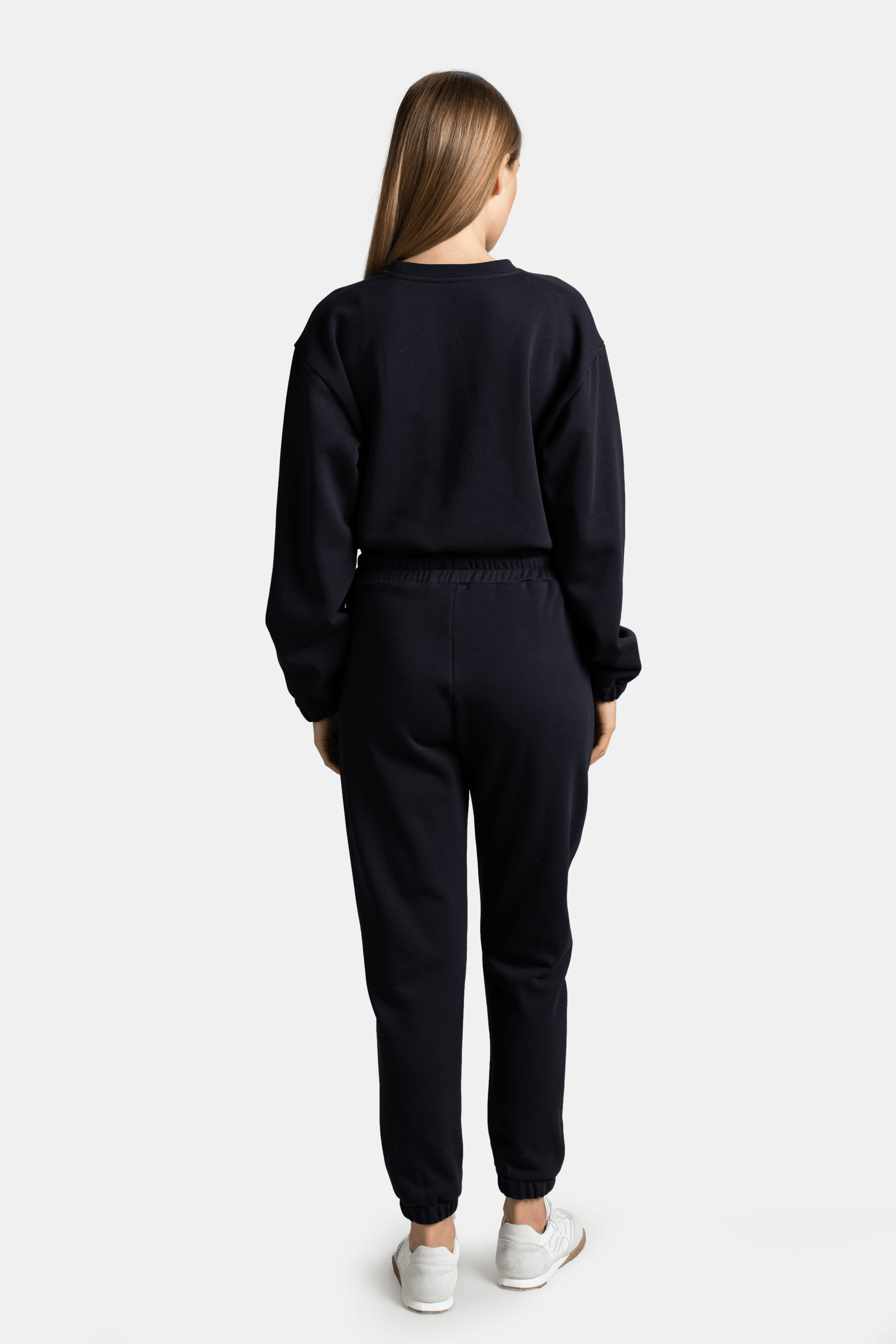 Back view of the black tracksuit set, showing the fit and design details from behind, with a relaxed posture.