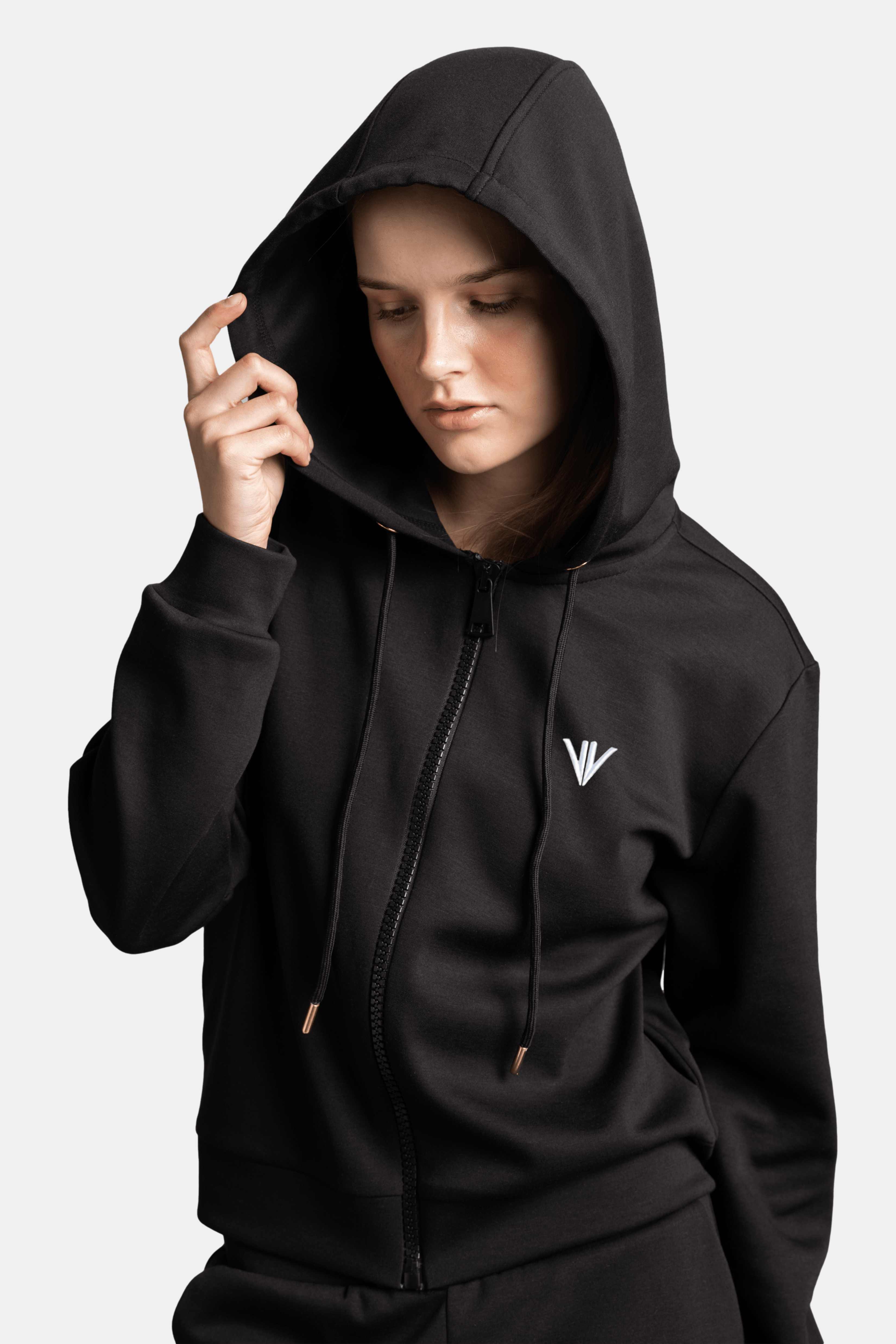 Close-up of the woman holding the edge of her hoodie’s hood, looking down, emphasizing the hoodie’s design details and texture.