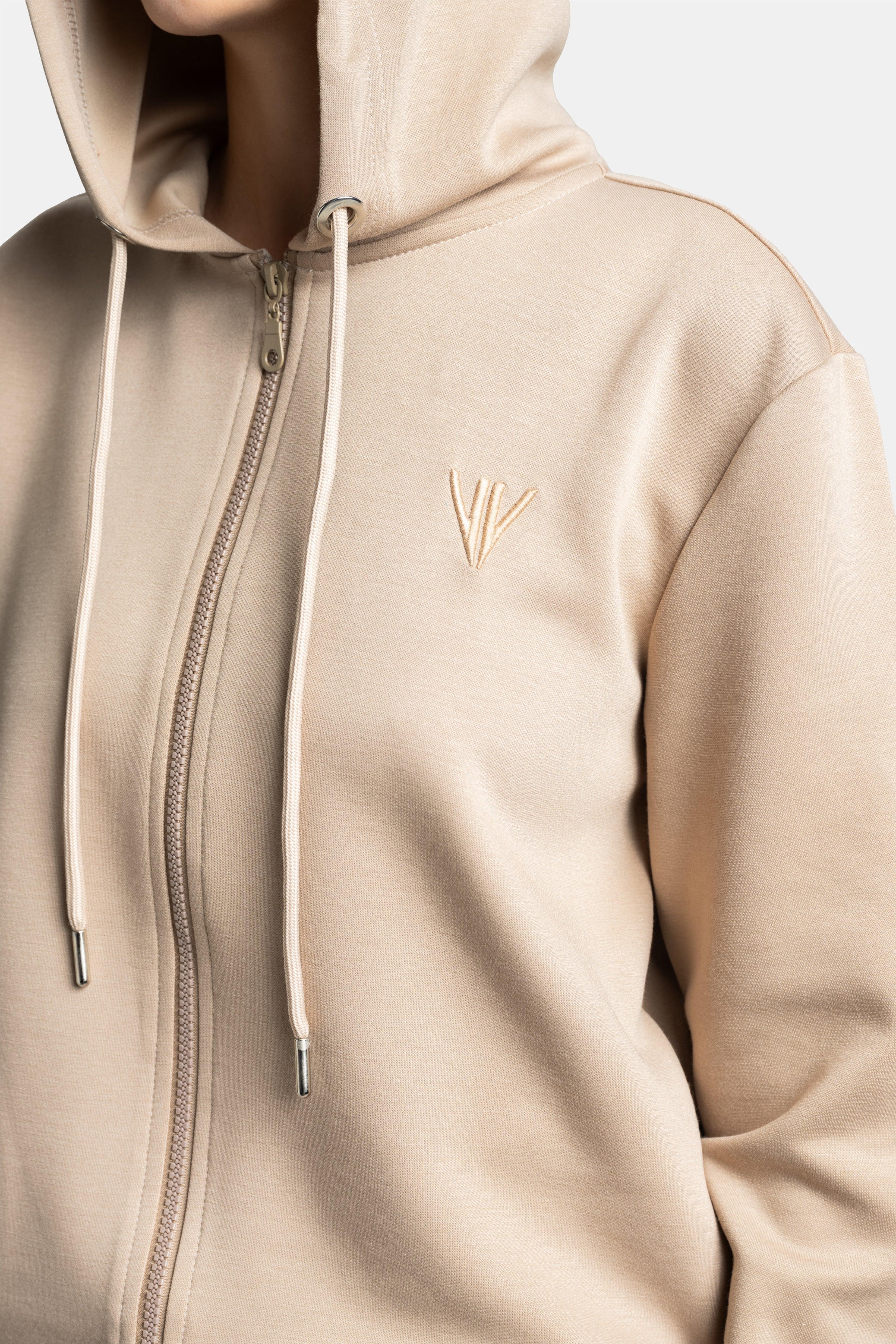 Detailed shot of the beige hoodie with a small embroidered logo, highlighting the texture and quality of the fabric.