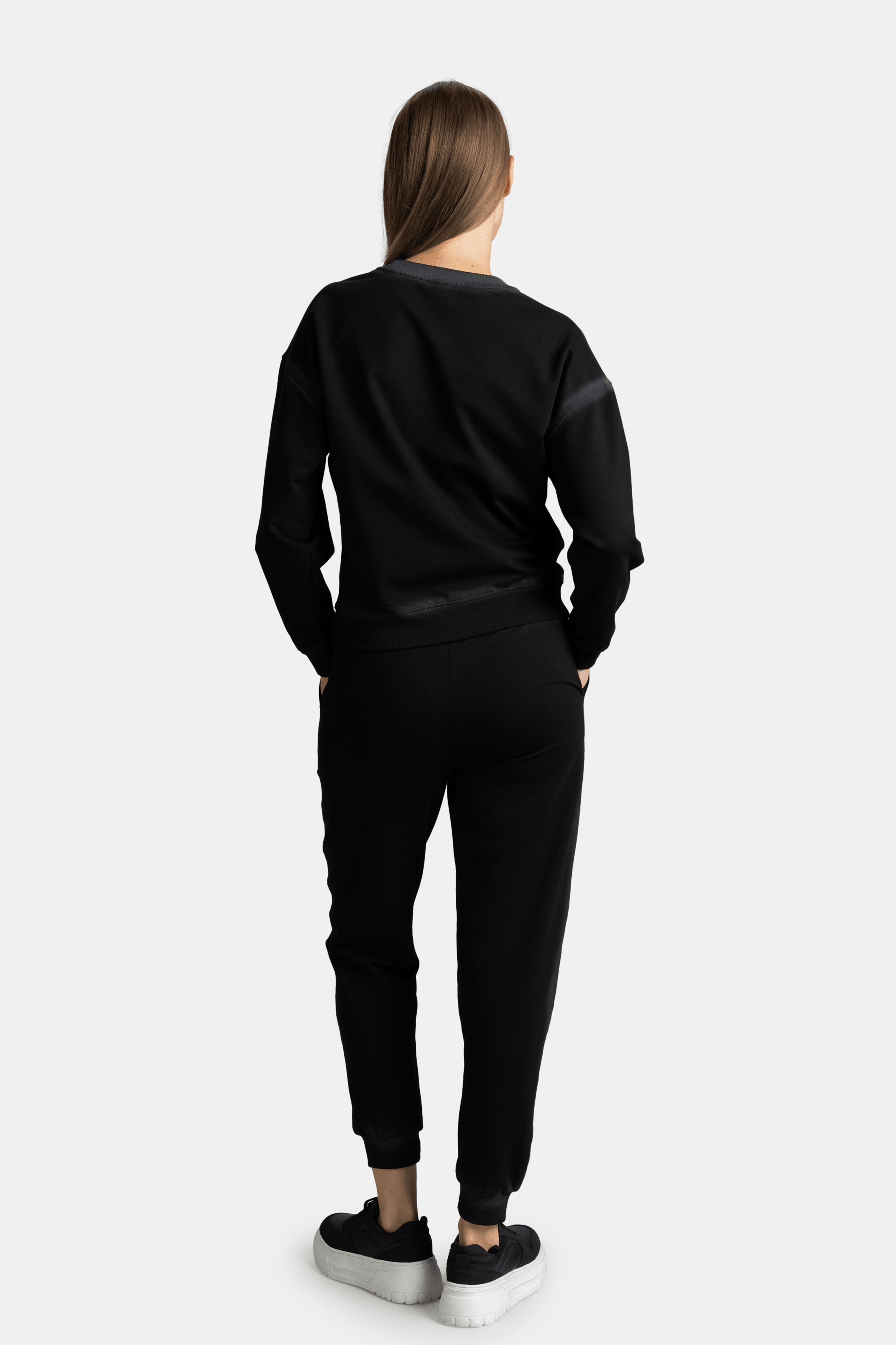 Back view of the model in a black sweatshirt and joggers, hands in pockets, showcasing the fit from behind.