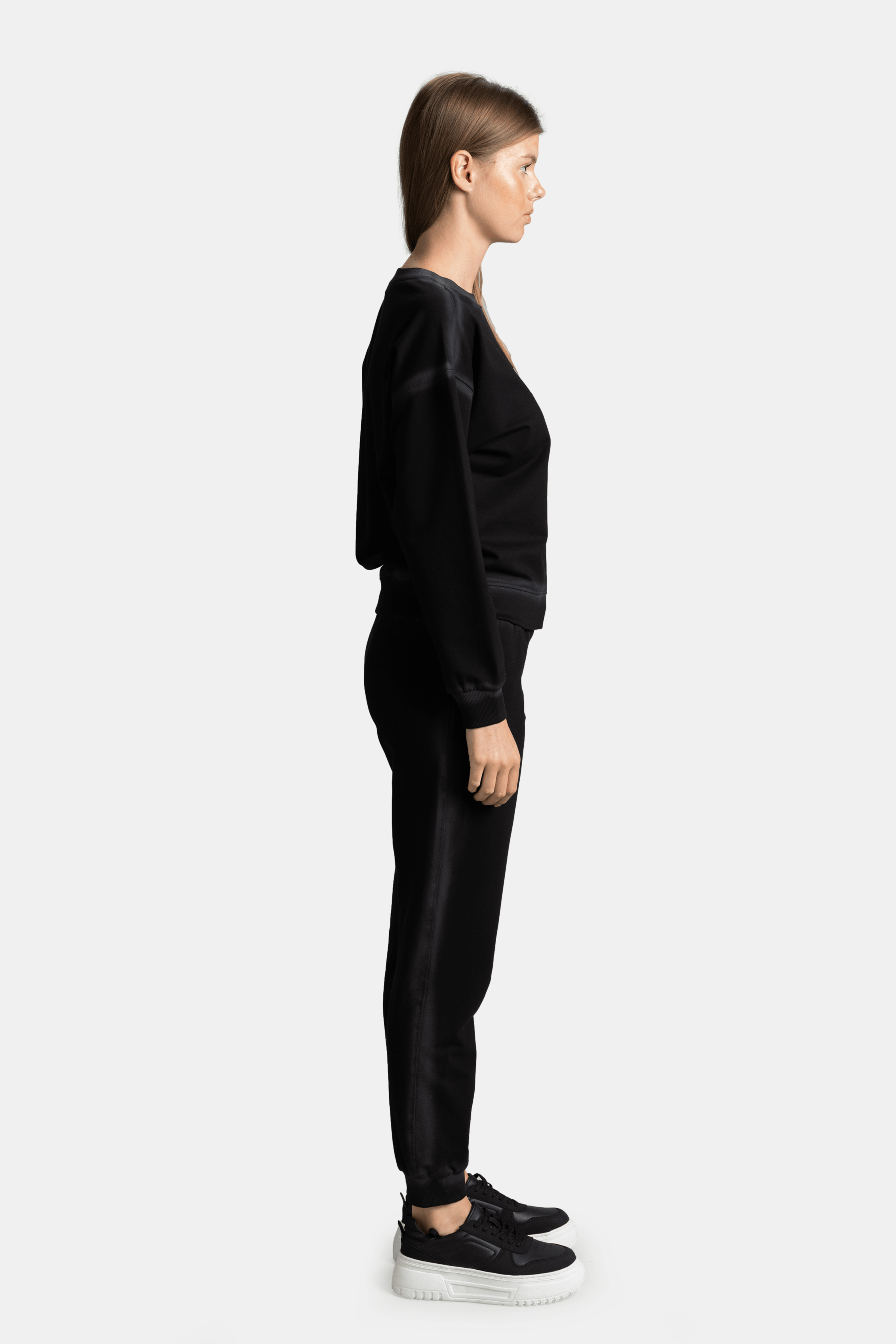 Side profile of the model in a black sweatshirt and jogger set, standing with a neutral expression.