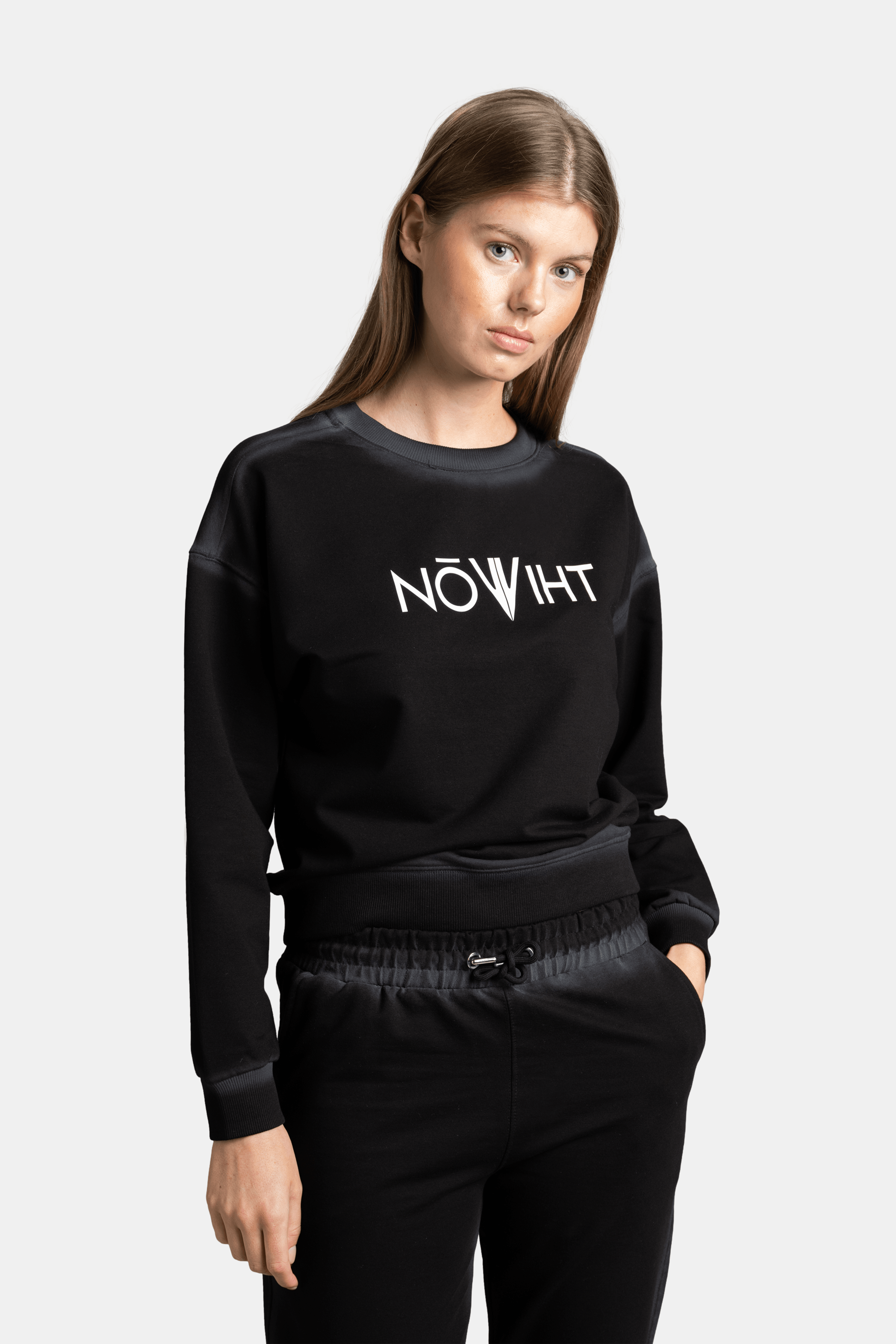 Close-up side angle of the model in a black sweatshirt with a white logo, with hands in pockets and looking to the side.