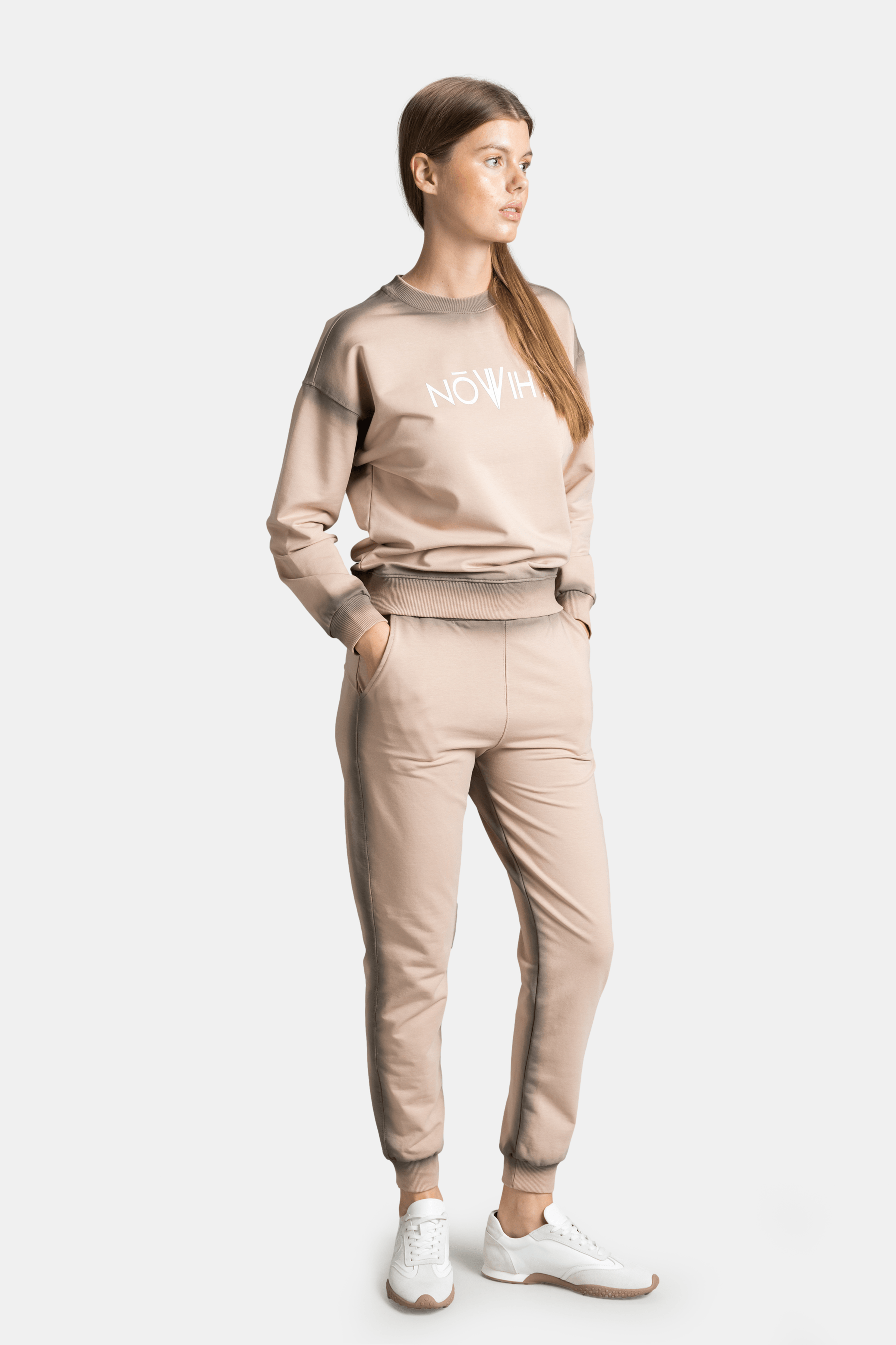 Side view of model in beige tracksuit, hands in pockets, showcasing the profile fit.