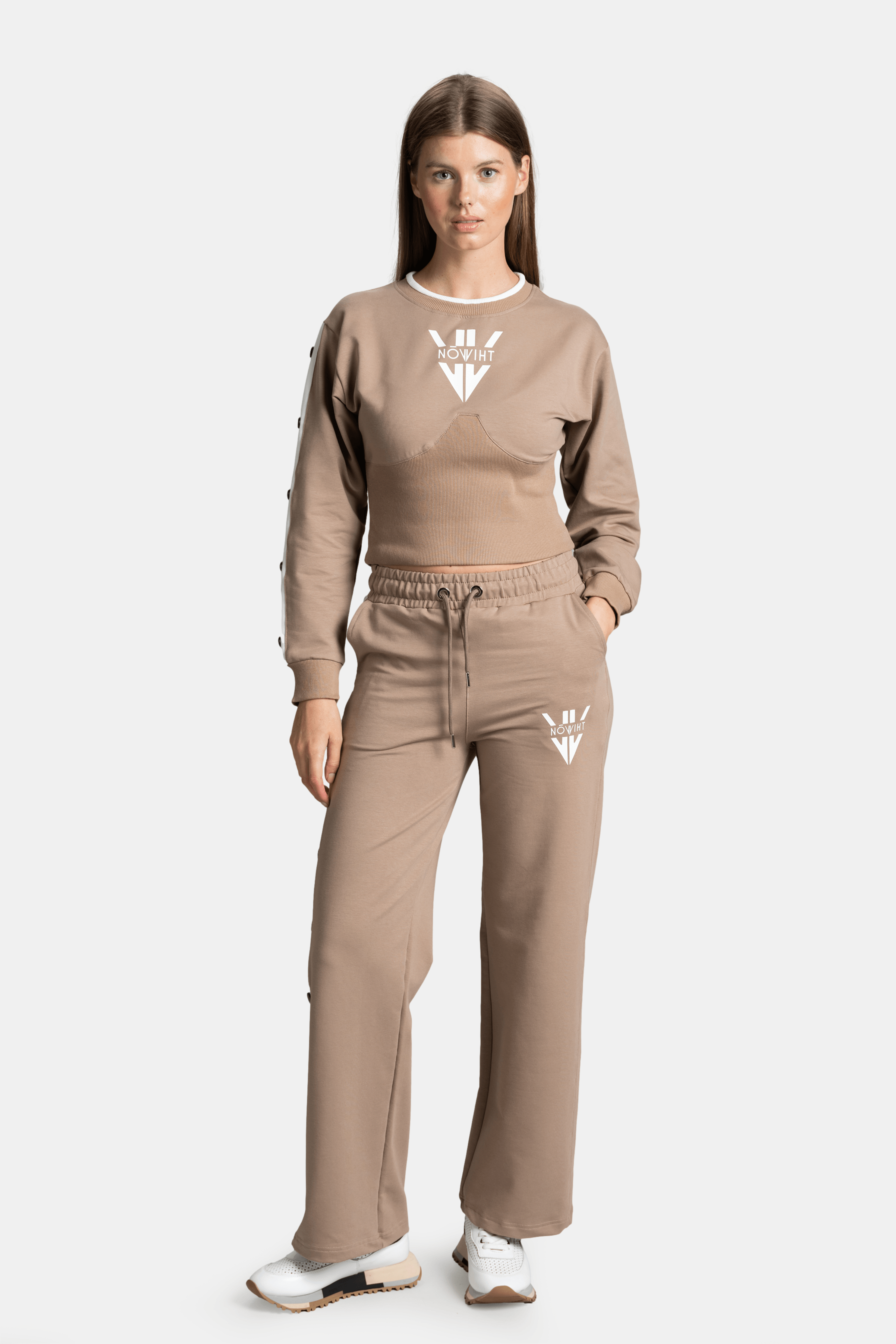 Front view of a beige tracksuit set with a cropped long-sleeve top and drawstring pants, featuring logo detail on the top and pants.