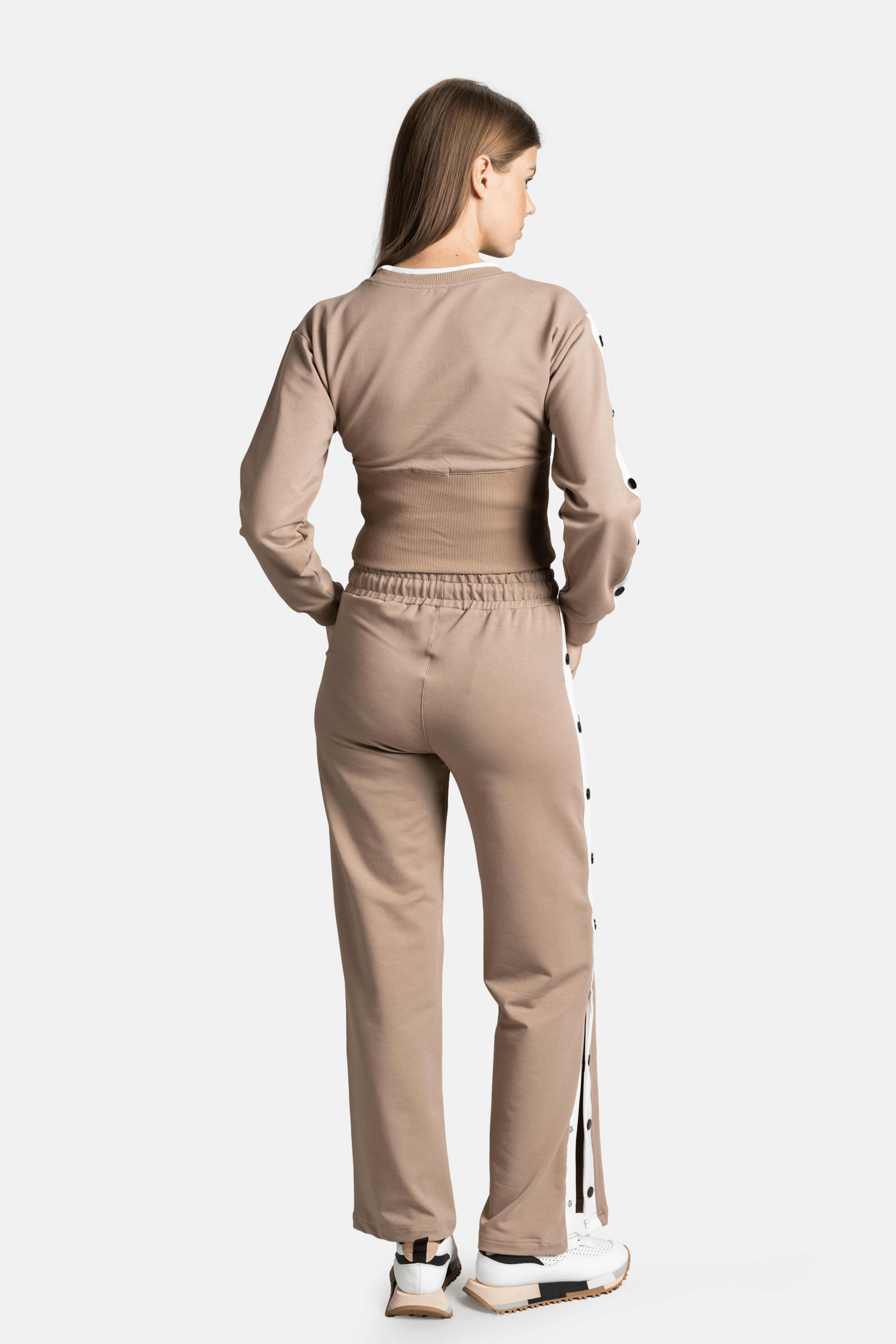 Back view of a beige tracksuit set with long sleeves and a wide-leg design, showing button details along the side.