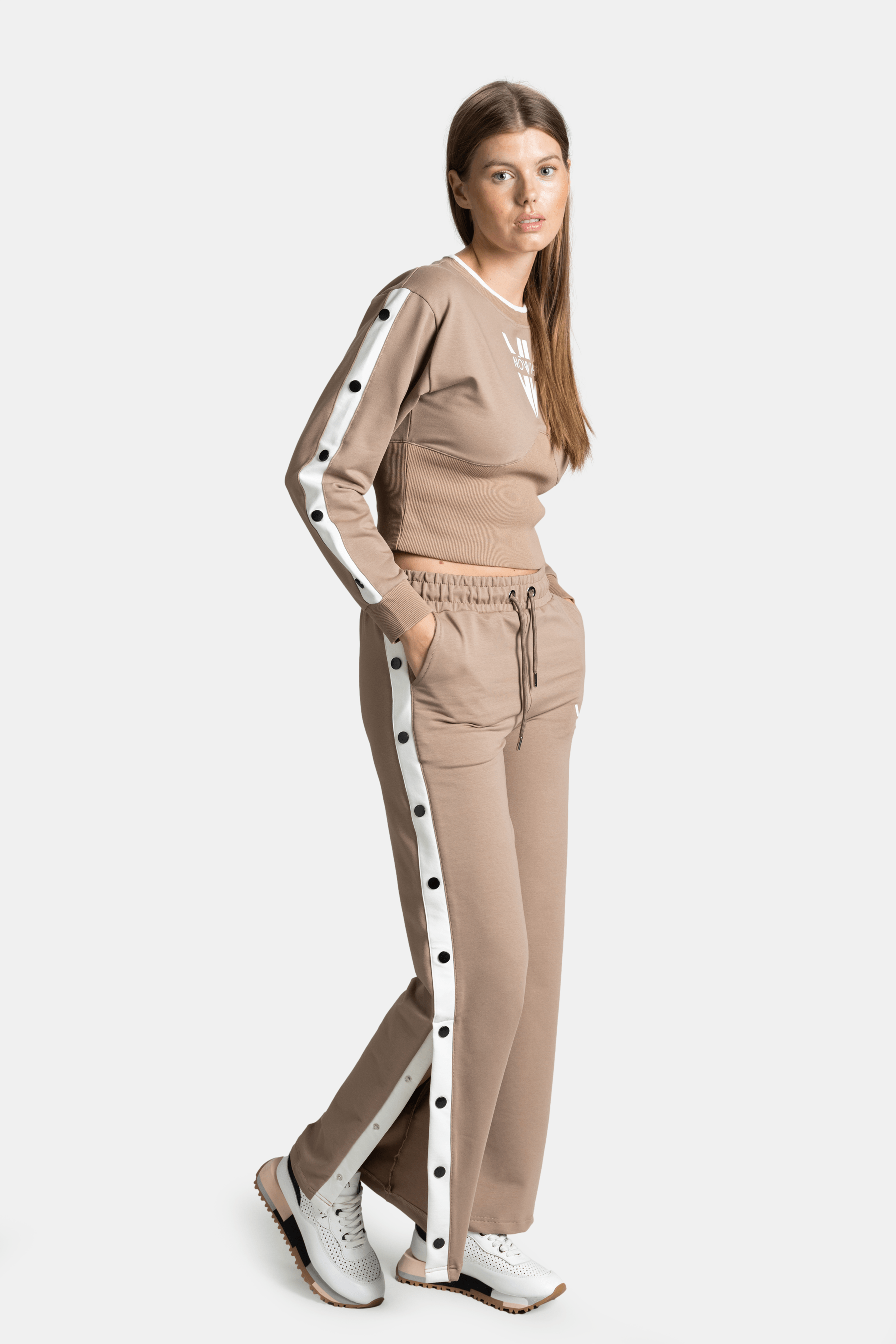 Side profile of a model wearing a beige tracksuit set, highlighting the button and stripe details along the sleeves and pants.