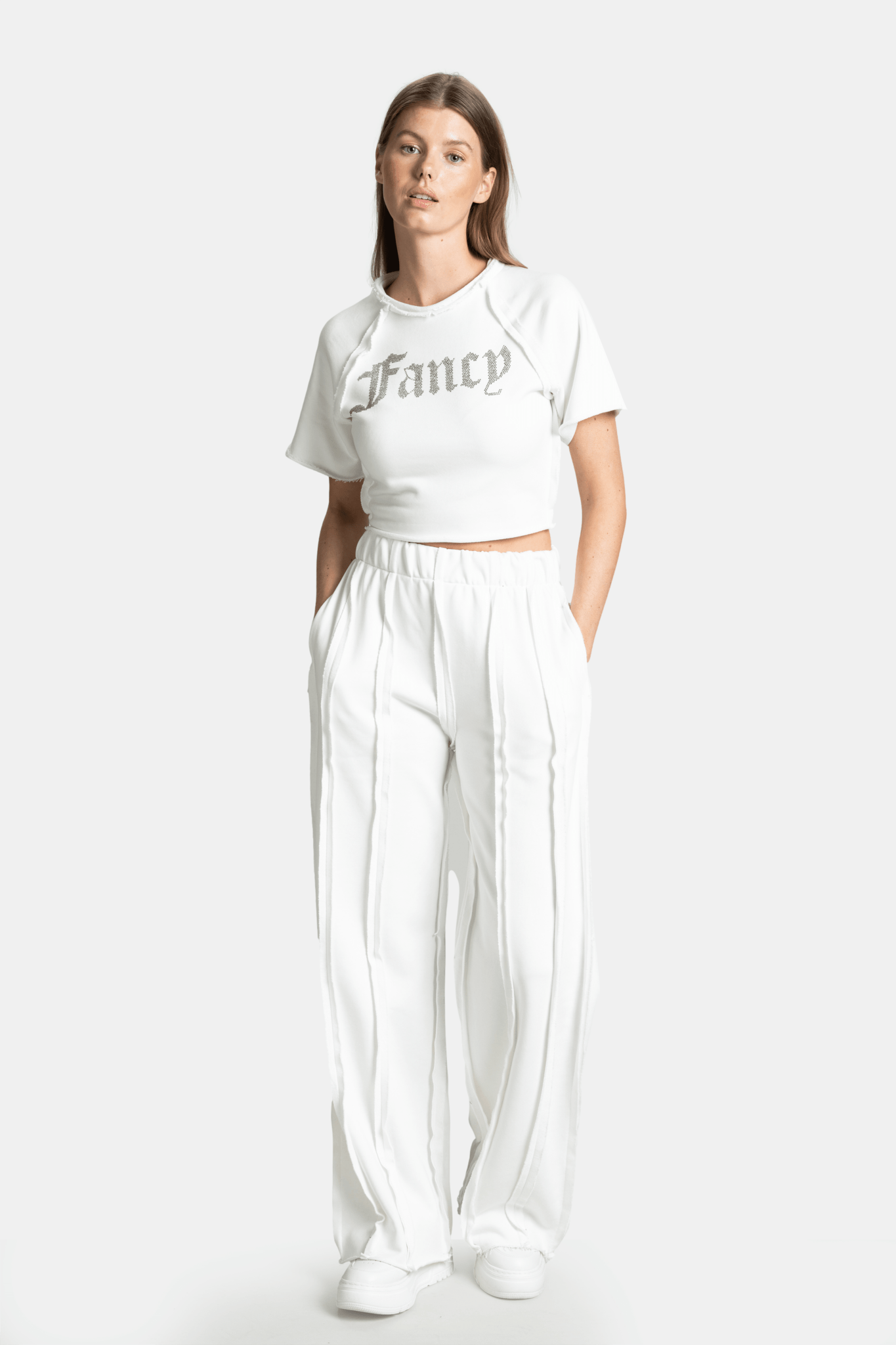 Model wearing the Amira Fancy Crop Tracksuit Set in Ecru, front view with hands in pockets.