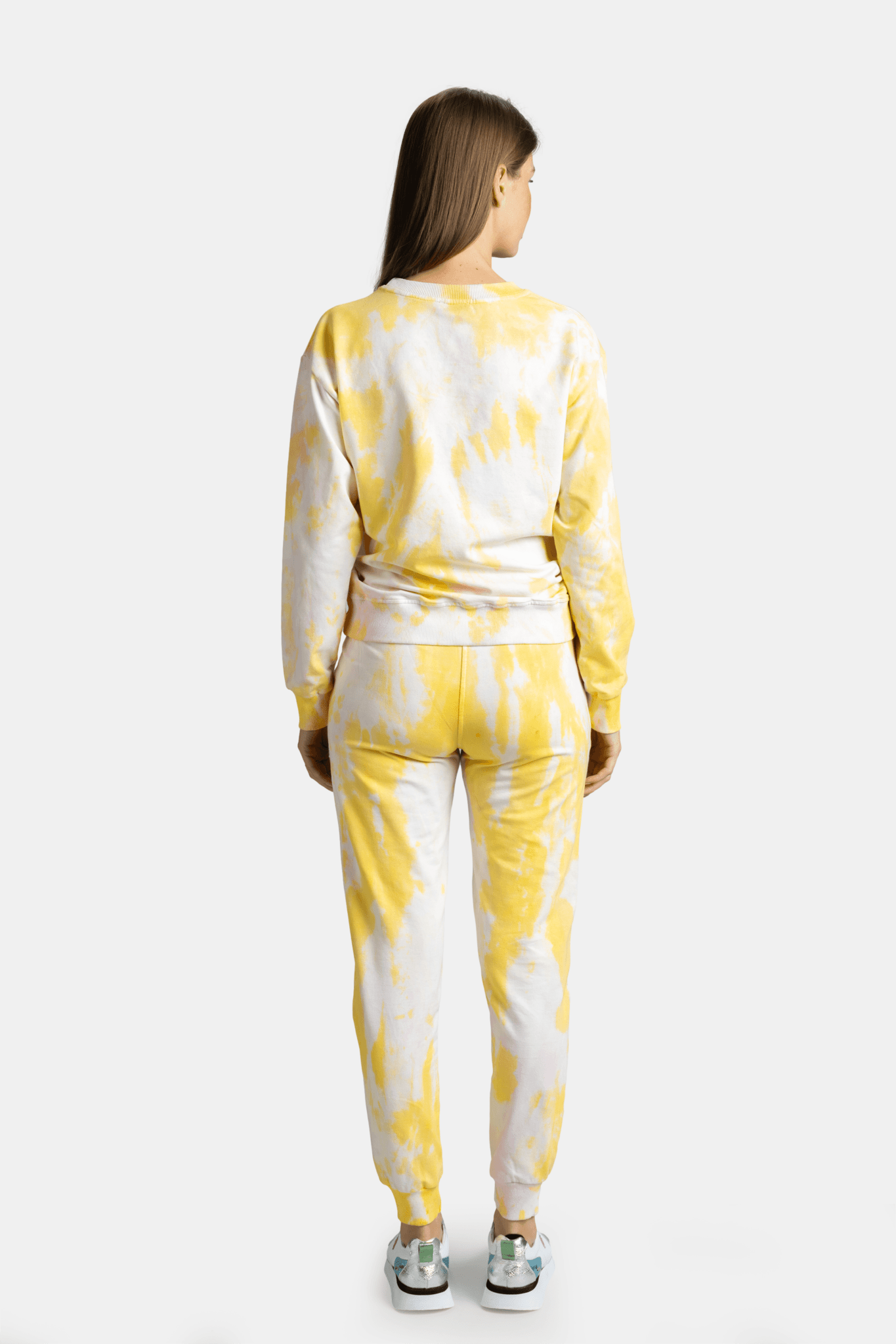 Rear view of a woman wearing a yellow tie-dye tracksuit, with her hands relaxed by her sides.