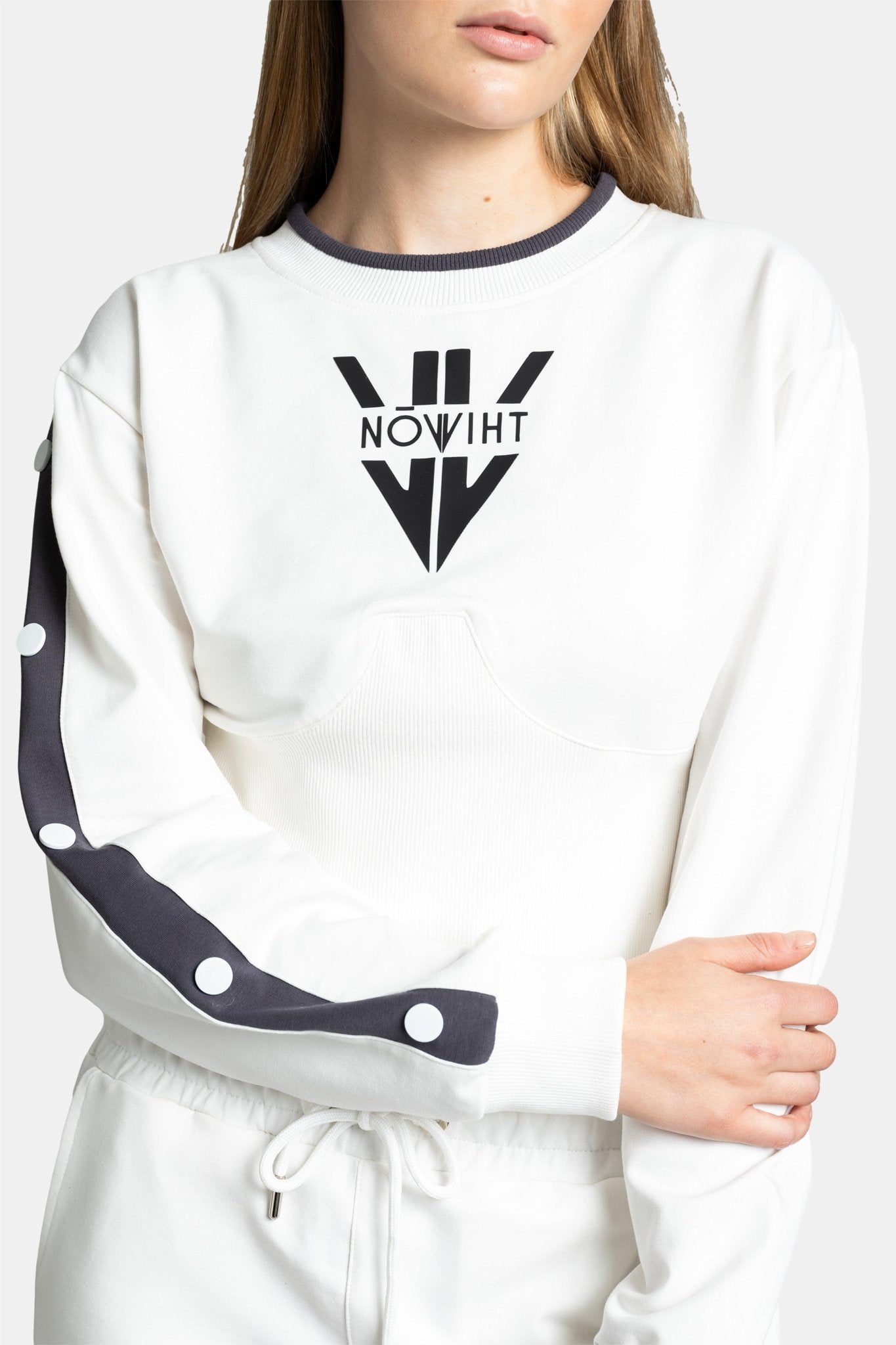 Model standing in a white tracksuit with black side details, hands by her sides, looking to her left.