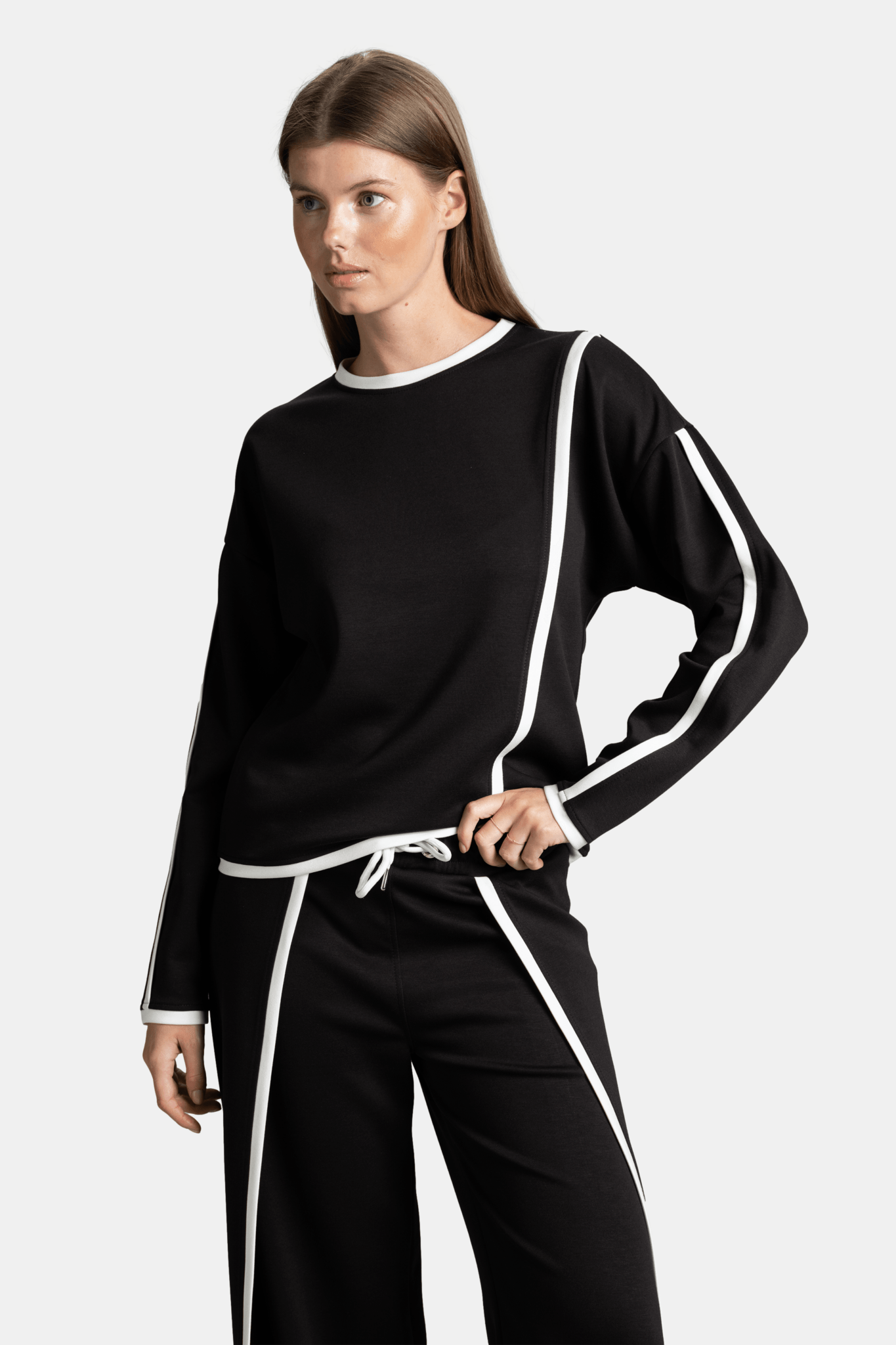 Side view of a woman wearing a black long-sleeve top with white trim, showcasing the unique asymmetrical design on the top.