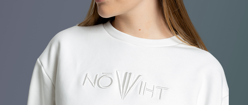 Close-up of NOWIHT embroidered logo on a white tracksuit sweatshirt, showcasing minimalist branding and modern sportswear style